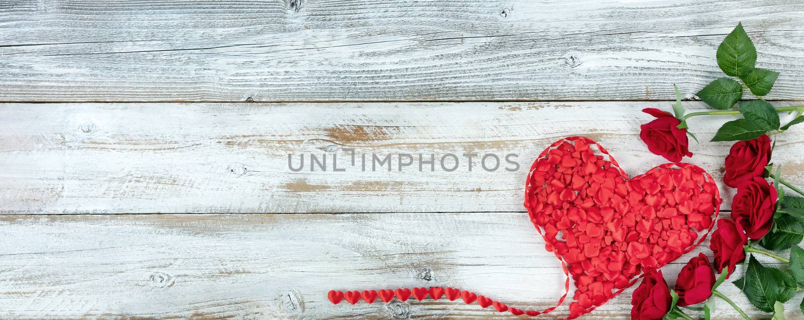 Romantic red roses and filled heart shaped ribbon on white rustic wooden background