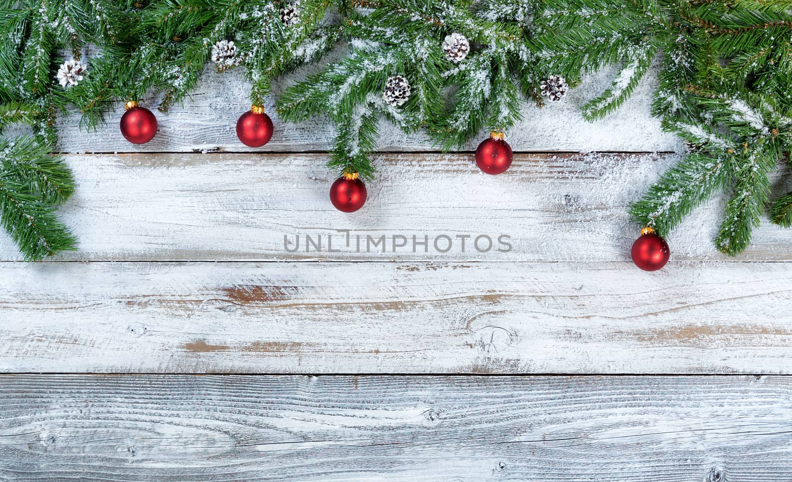 Snowy Christmas fir branches with traditional red ball ornaments and pine cones on rustic wood in flat lay format