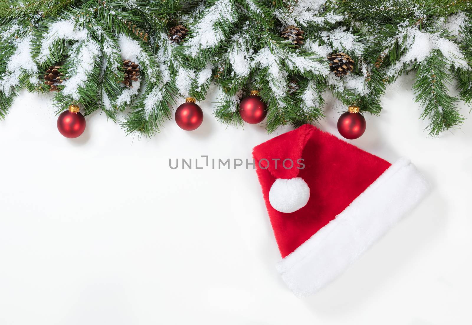 Christmas snowy tree branches, red ornaments and Santa Claus hat on white background