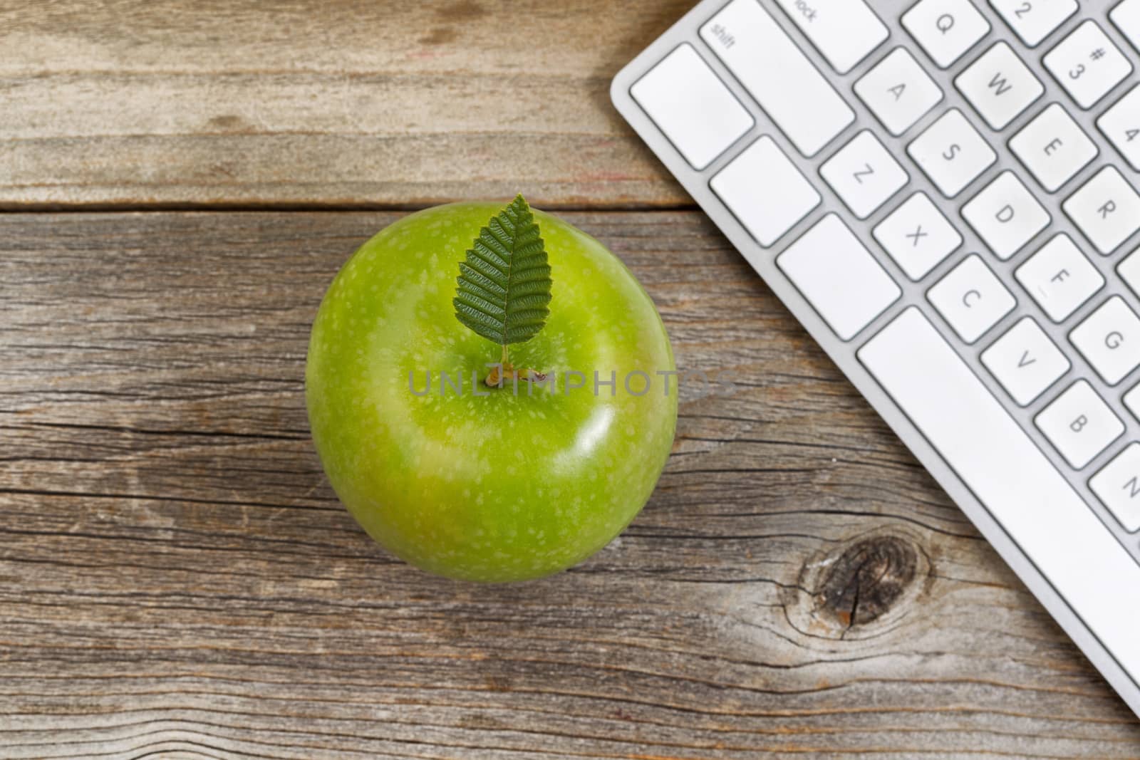 Top view of green apple, selective focus on top leaf, with partial computer keyboard on rustic wood.