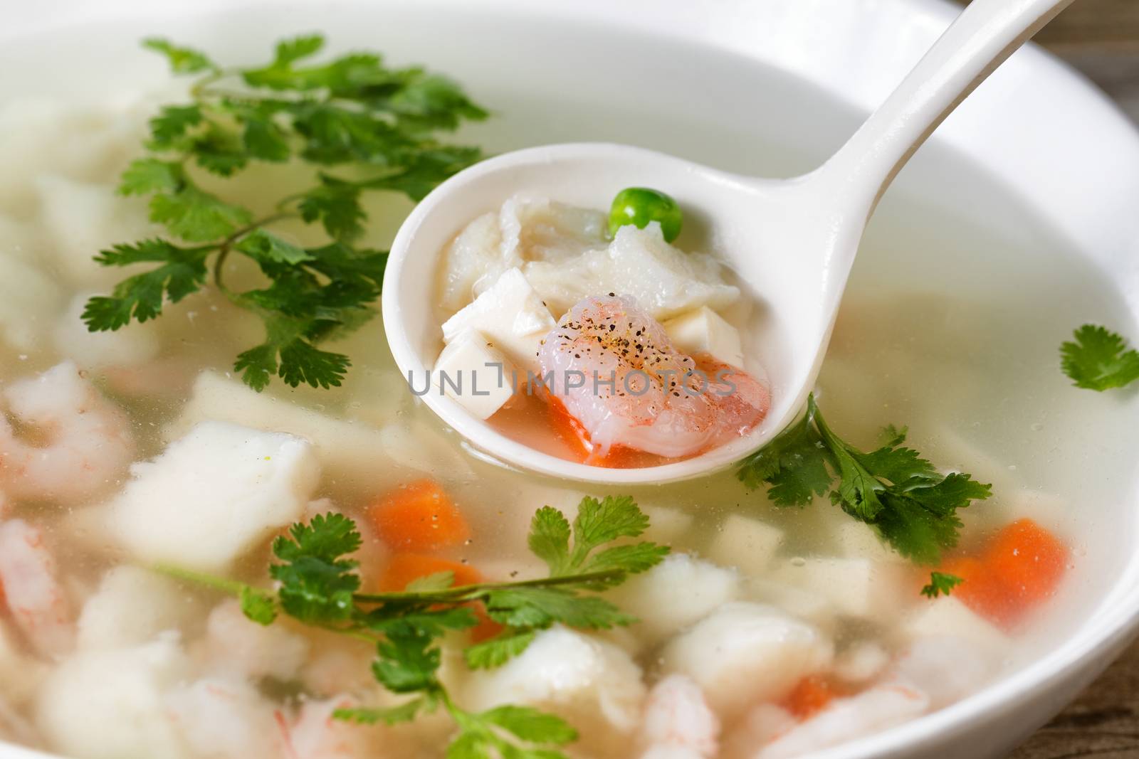 Close up shrimp and fish, selective focus on single piece in spoon, soup in bowl. 