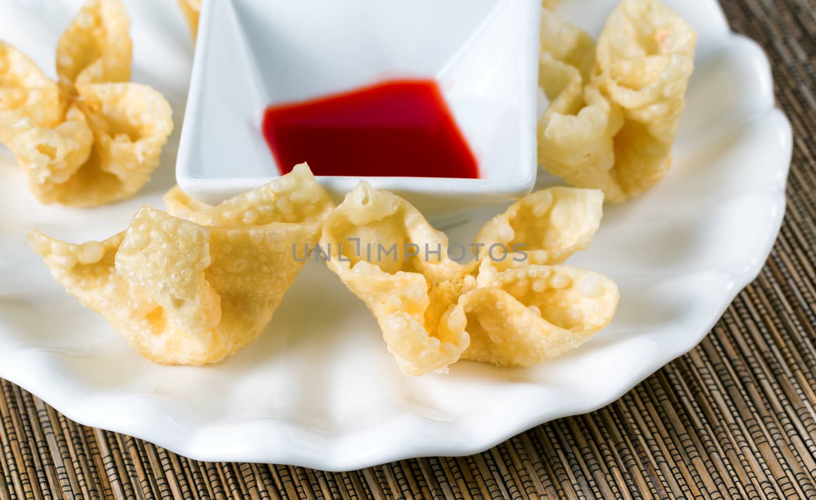 Close up view of crispy fried wanton treats with dipping sauce in background. Selective focus on front shells. 