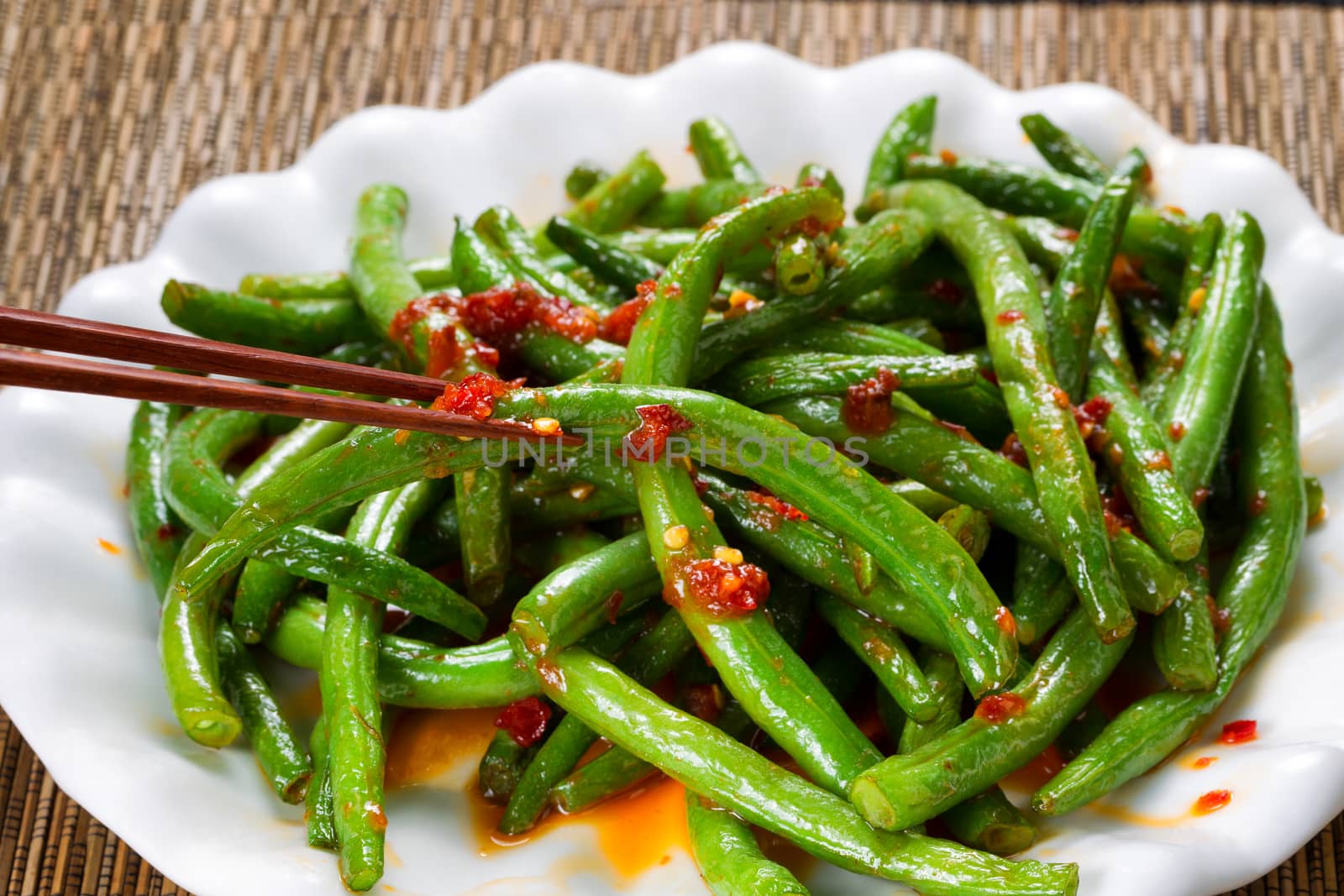 Close up view of spicy green beans with chopsticks in use. Selective focus on single bean being held by chopsticks. 