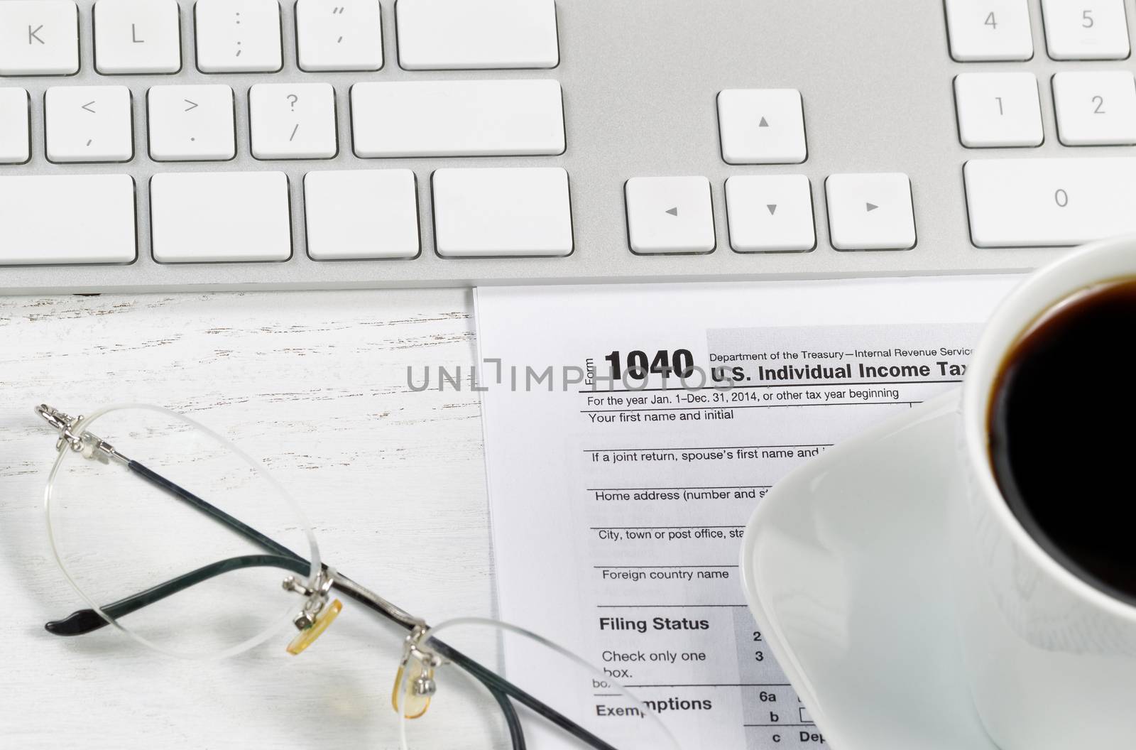 Close up of tax form, reading glasses, computer keyboard and coffee on white desk. Focus on Tax form 1040. 