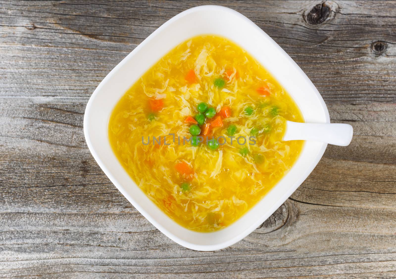High angled view of egg and vegetable soup with spoon in bowl on rustic wood. 