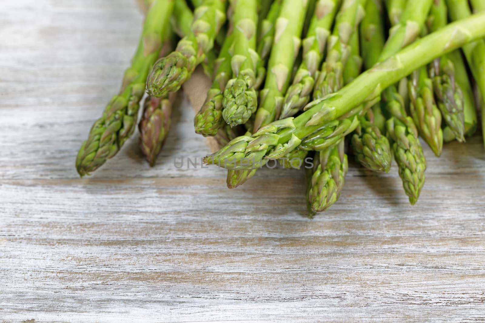 Close up of pile of asparagus; focus on front with shallow depth of field, on rustic white wood 