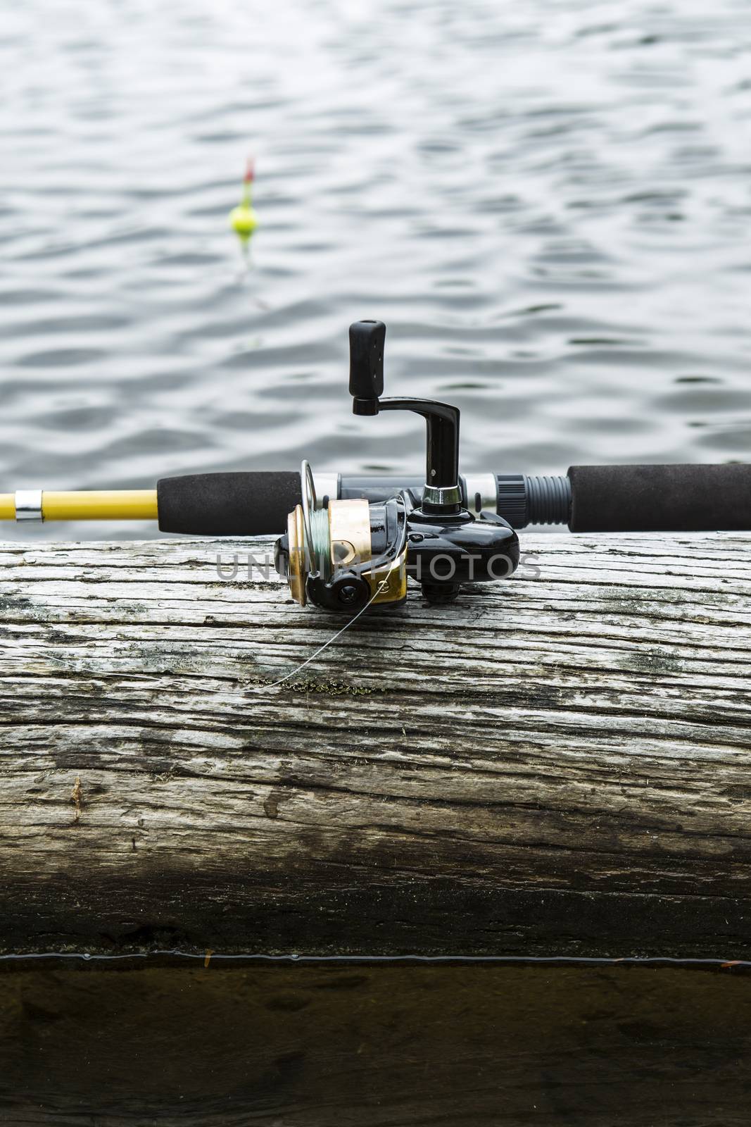 Fishing reel, rod on log with water and bobber in background 
