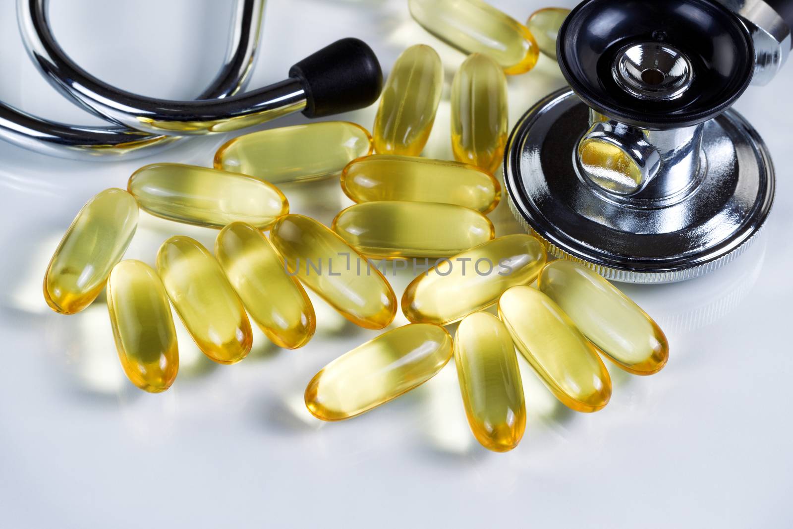 
Fish oil omega 3 gel capsules with stethoscope on white background with reflection.
