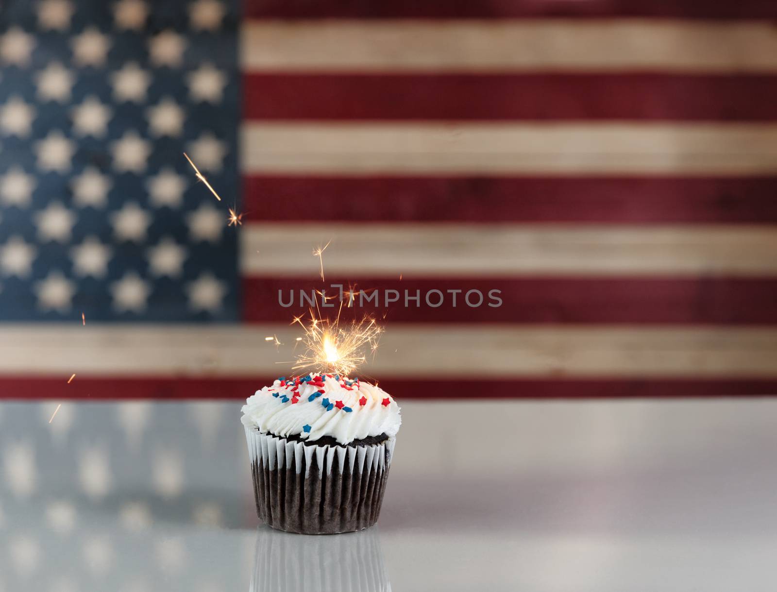 Chocolate cupcake and exploding sparkler with rustic wooden United States Flag in background. July 4th holiday concept