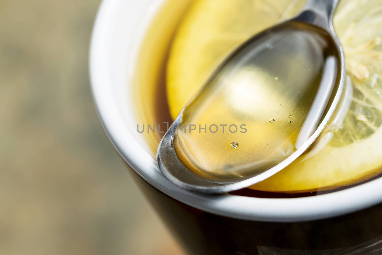 Horizontal closeup photo of golden honey, in spoon, with fresh lemon slice in hot cup of tea