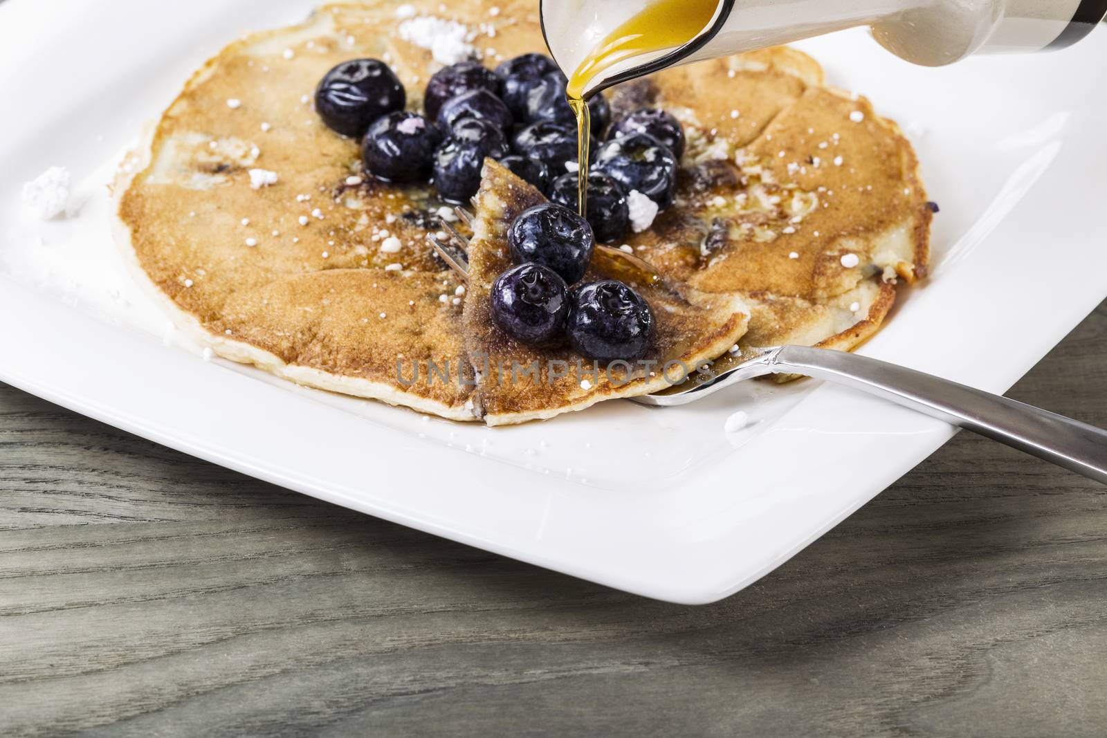 Pure maple syrup being poured onto freshly made pancakes with blueberries on top 