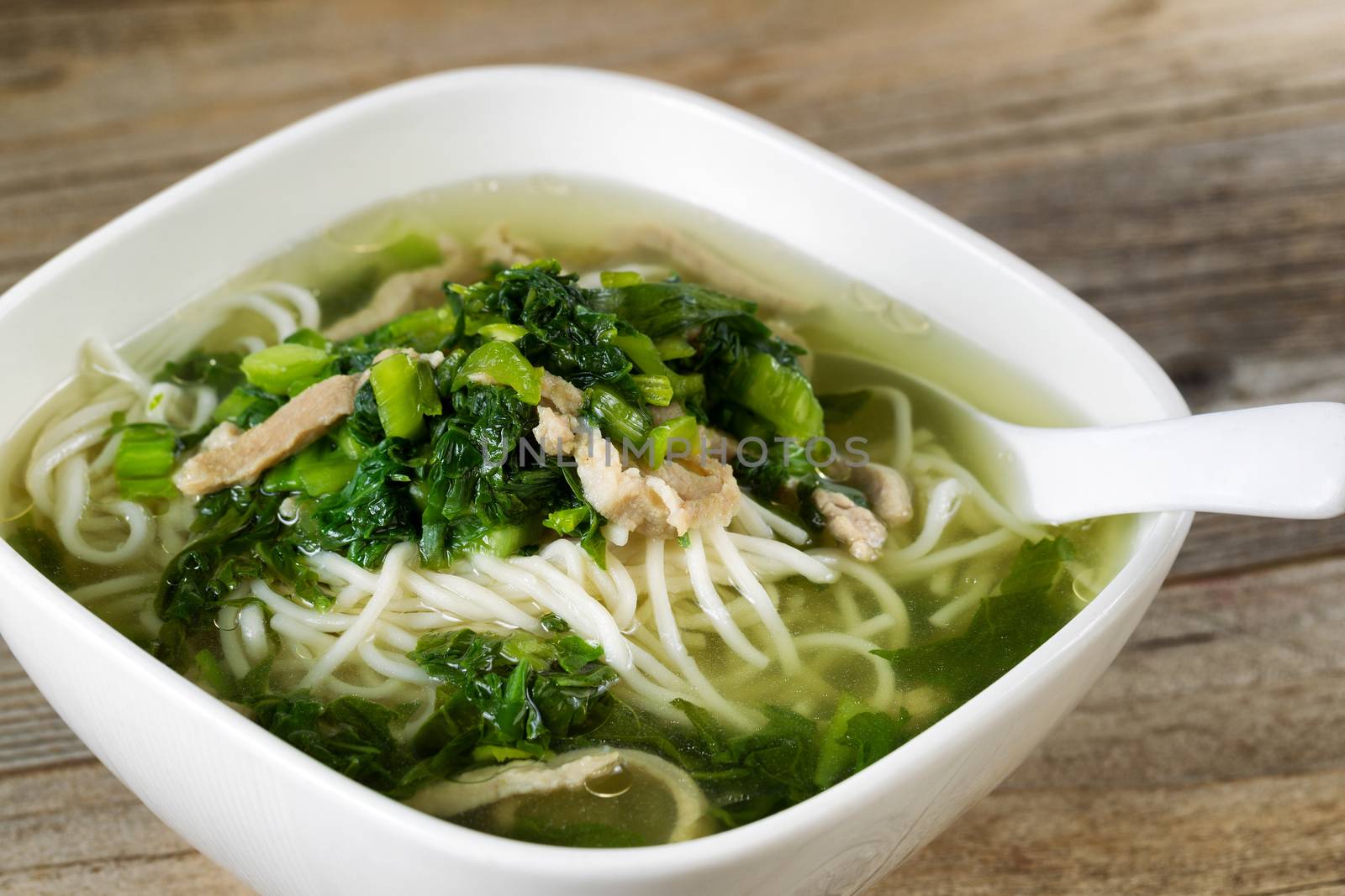 Close up noodle and vegetable soup with spoon in bowl on rustic wood. 