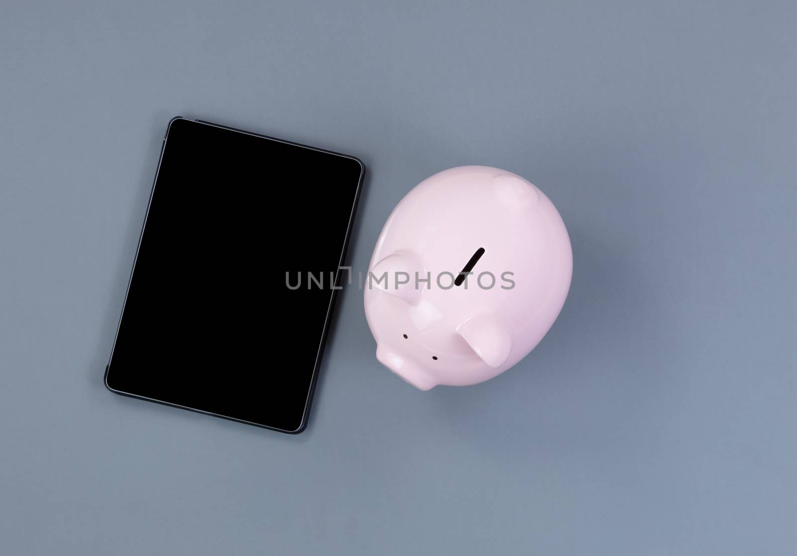 Piggy Bank and modern portable technology on gray desktop 