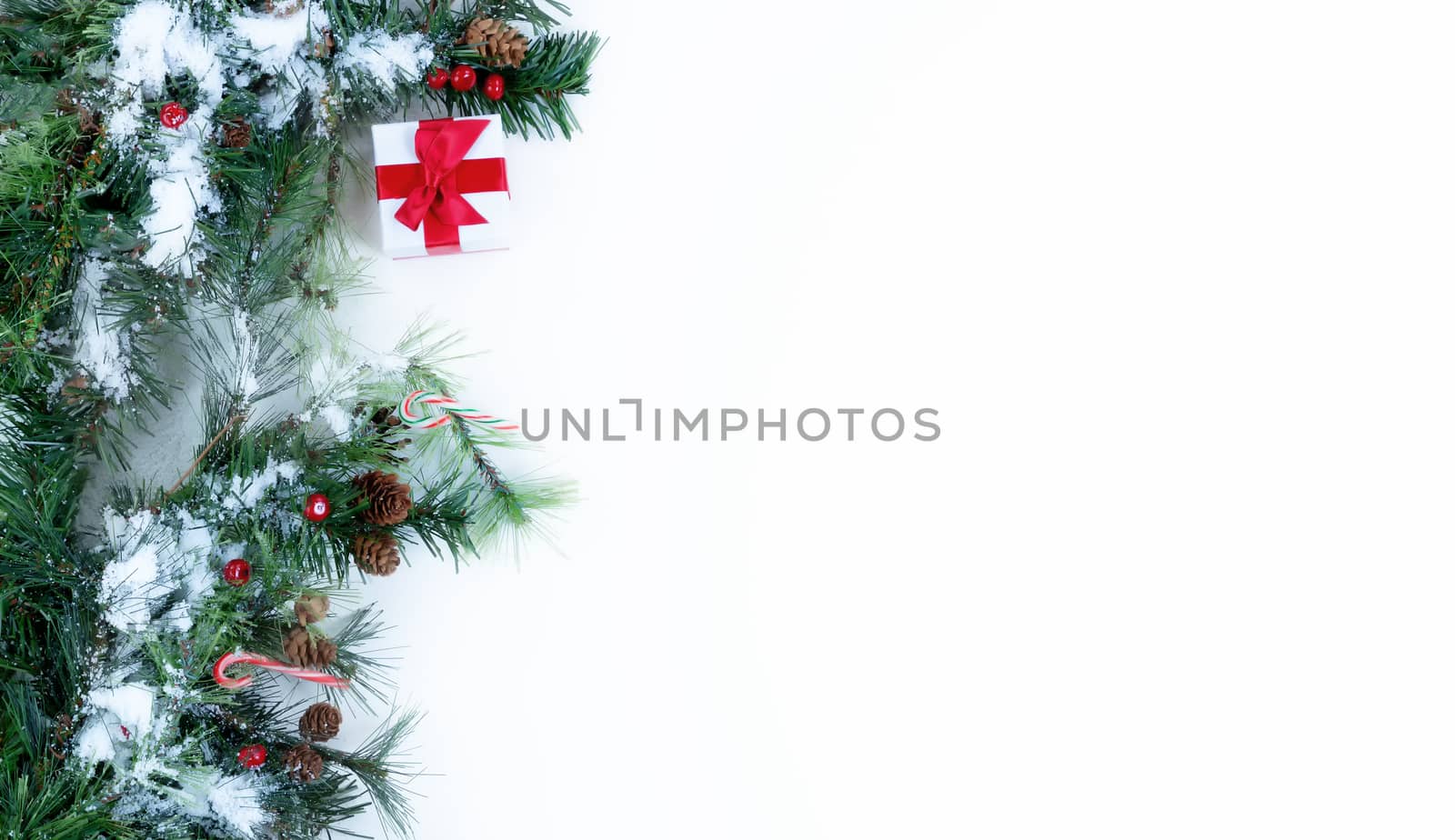 Snow on Christmas tree evergreen branches and decorations on left border of a white background  