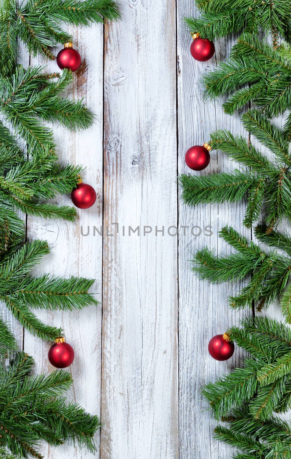 Christmas tree branches and red ornaments forming vertical borders on rustic white wood