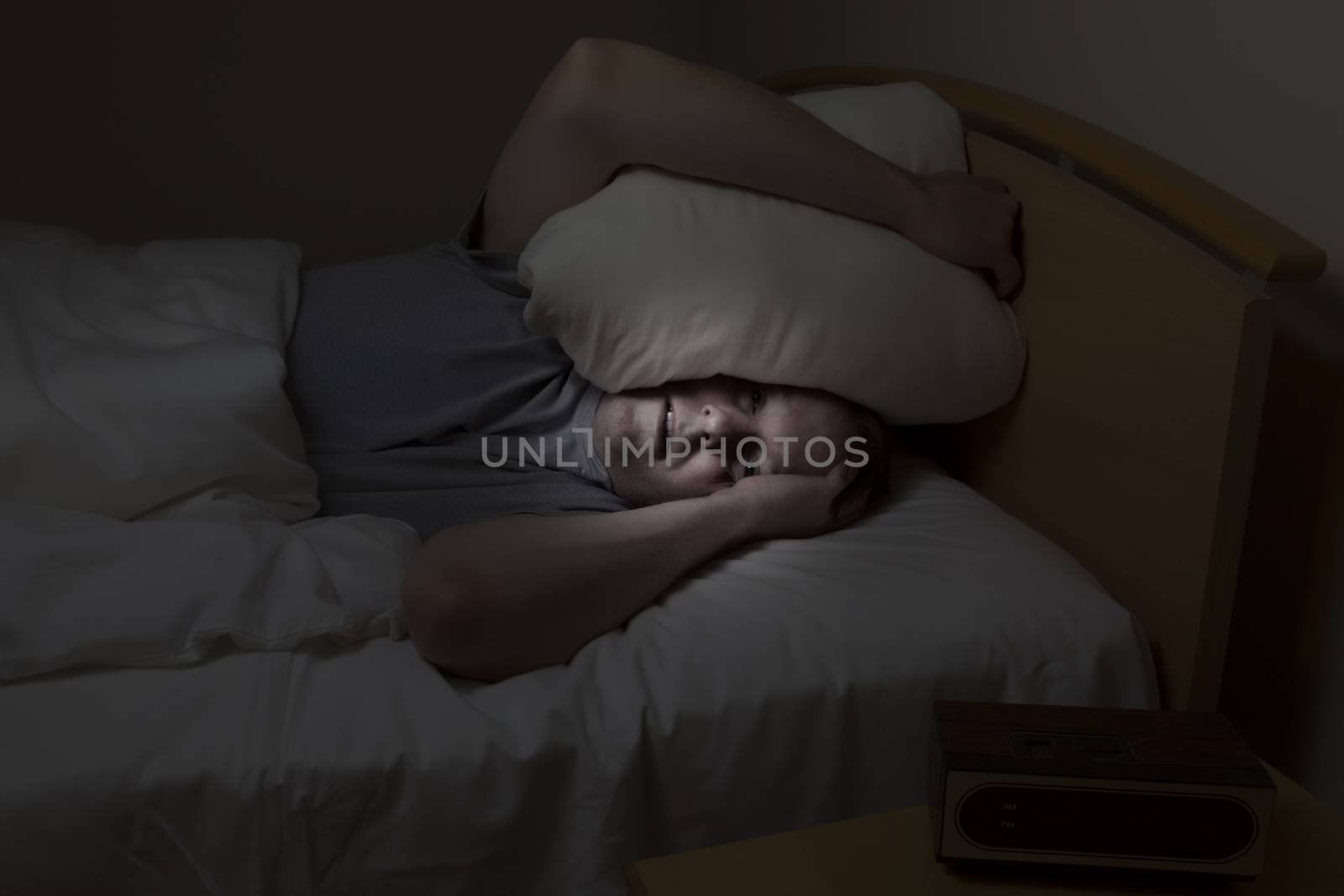 Mature man, pillow over head with eyes wide open, cannot sleep at night from insomnia