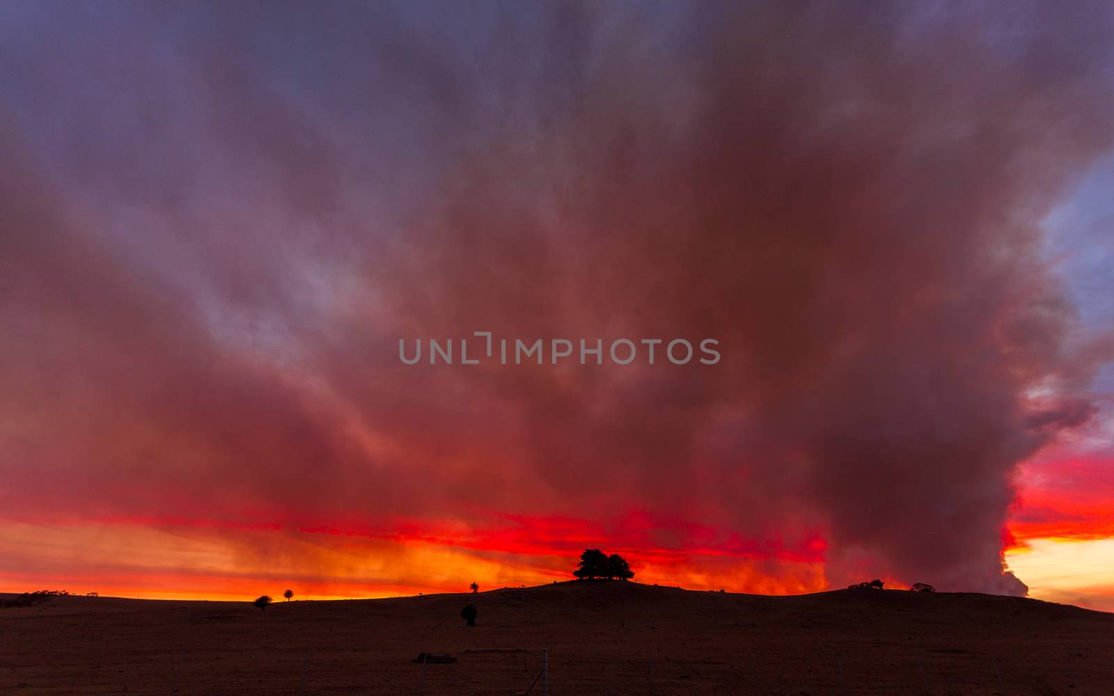 Looking back over farmlands and rural fields to the bush fire near Braidwood, Australia at dusk.