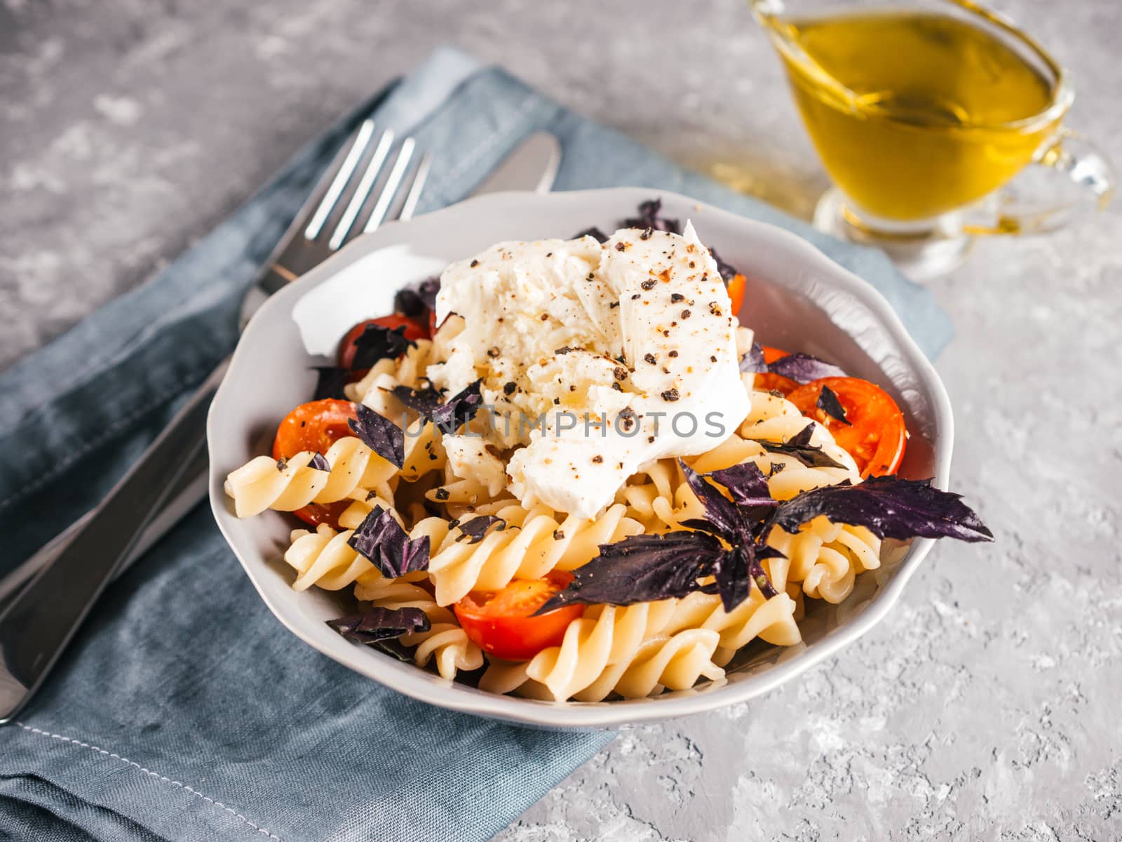 Tasty italian fusilli pasta with cherry, mozarella or buratta cheese and fresh basil. Dish with pasta on gray concrete background. Copy space. Healthy food concept and recipe idea.