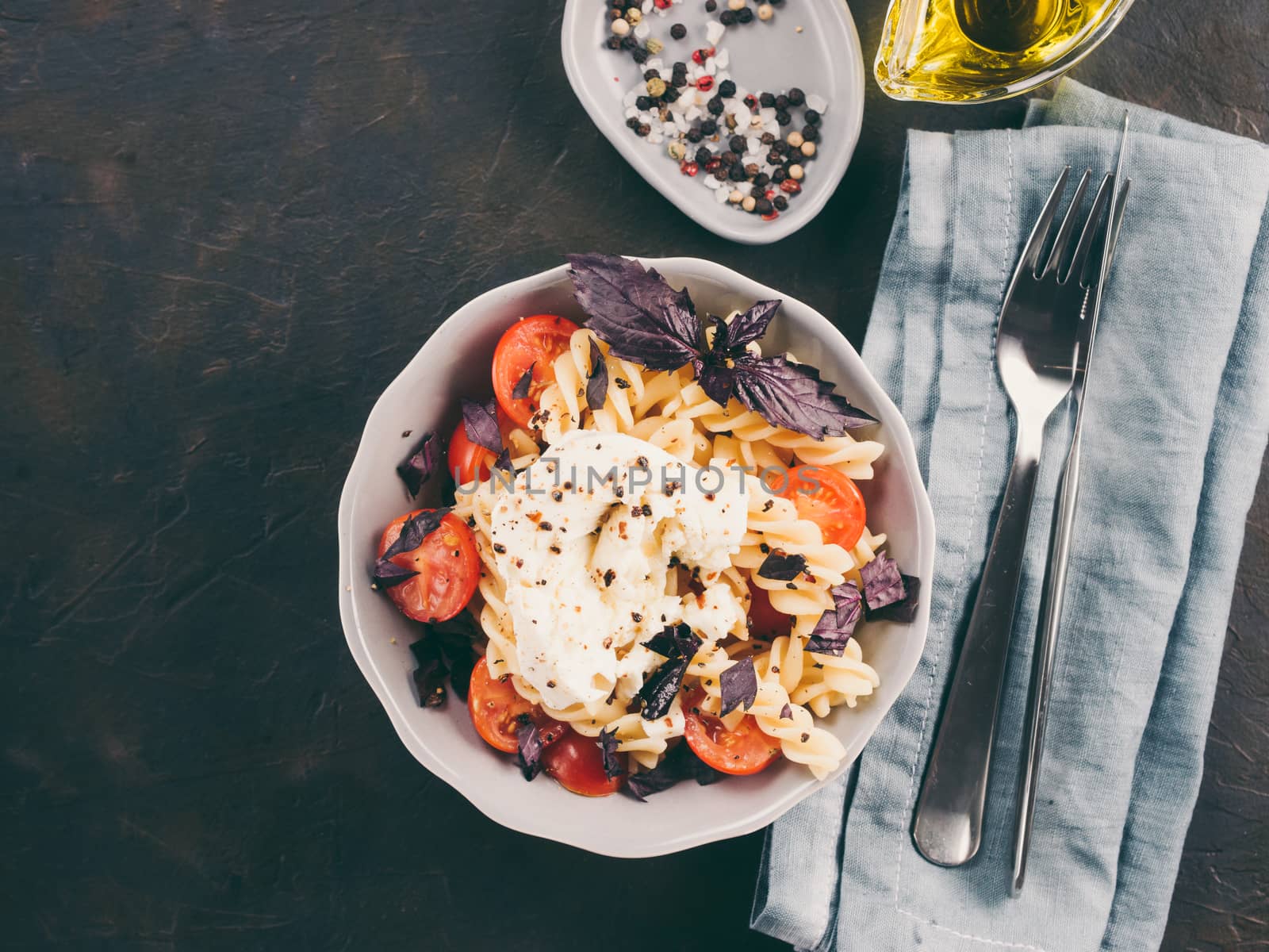 Tasty italian fusilli pasta with cherry, mozarella or buratta cheese and fresh basil. Dish with pasta on black concrete background. Top view. Copy space. Healthy food concept and recipe idea.