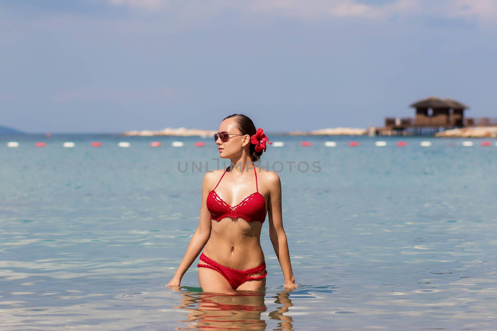 Beautiful woman walking in sea waterLovely young lady in red knitted swimwear looking away and walking in sea water while relaxing in wonderful resort