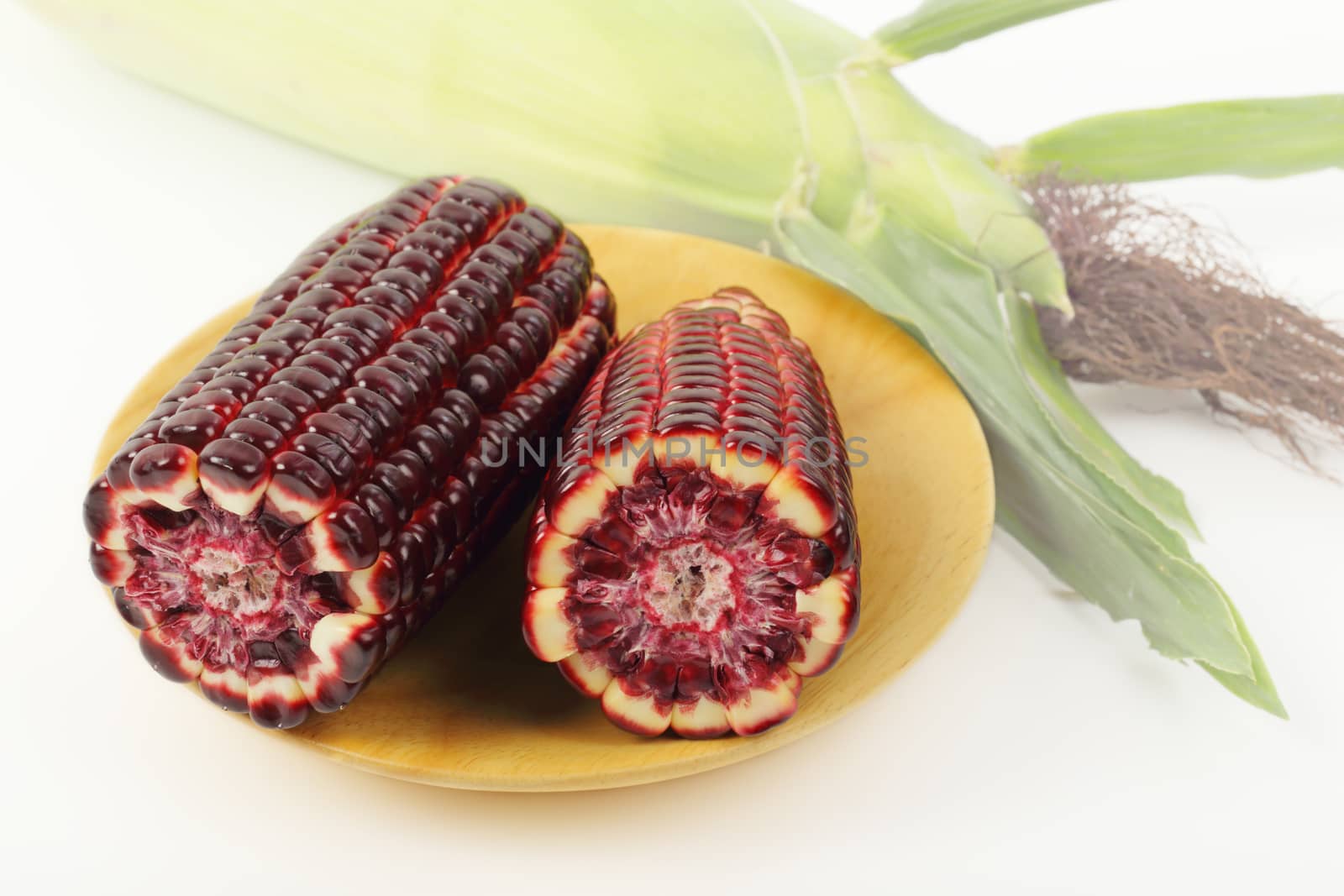 Fresh purple corn fruits isolated on wooden plate over white background. 