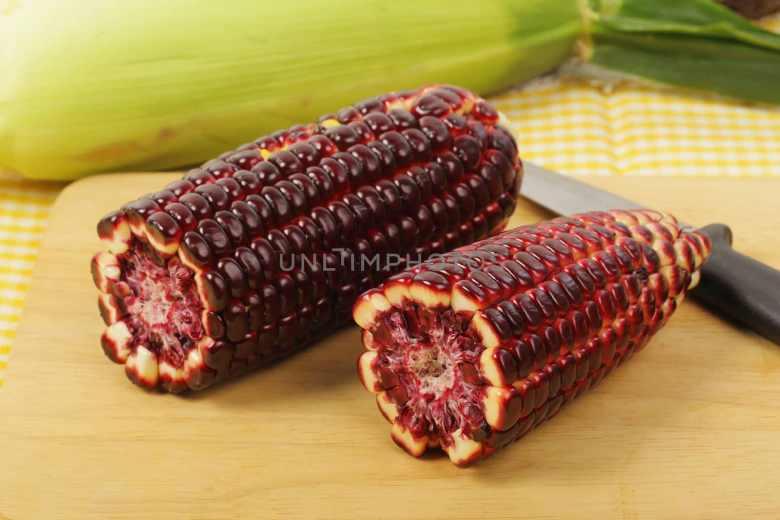 Fresh purple corn fruits on chopping board over napery background. 
