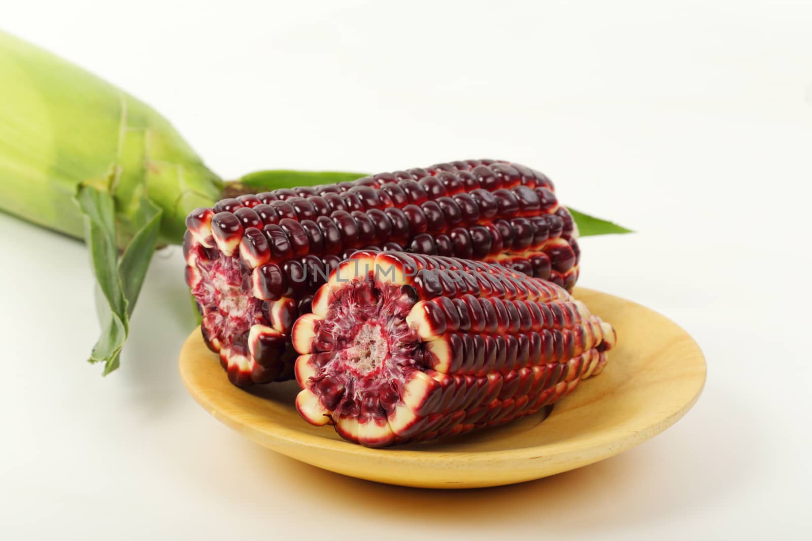 Fresh purple corn fruits isolated on wooden plate over white background. 