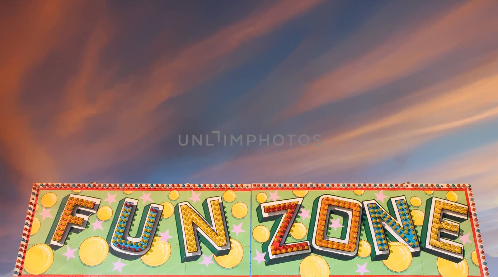 A colorful fun zone sign at a carnival against a blue sky