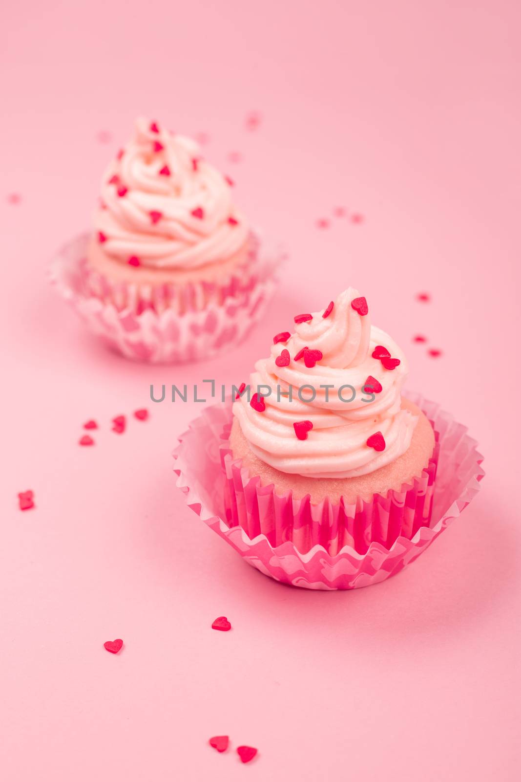 Valentine day two love cupcakes decorated with cream and hearts on pink background with copy space for text