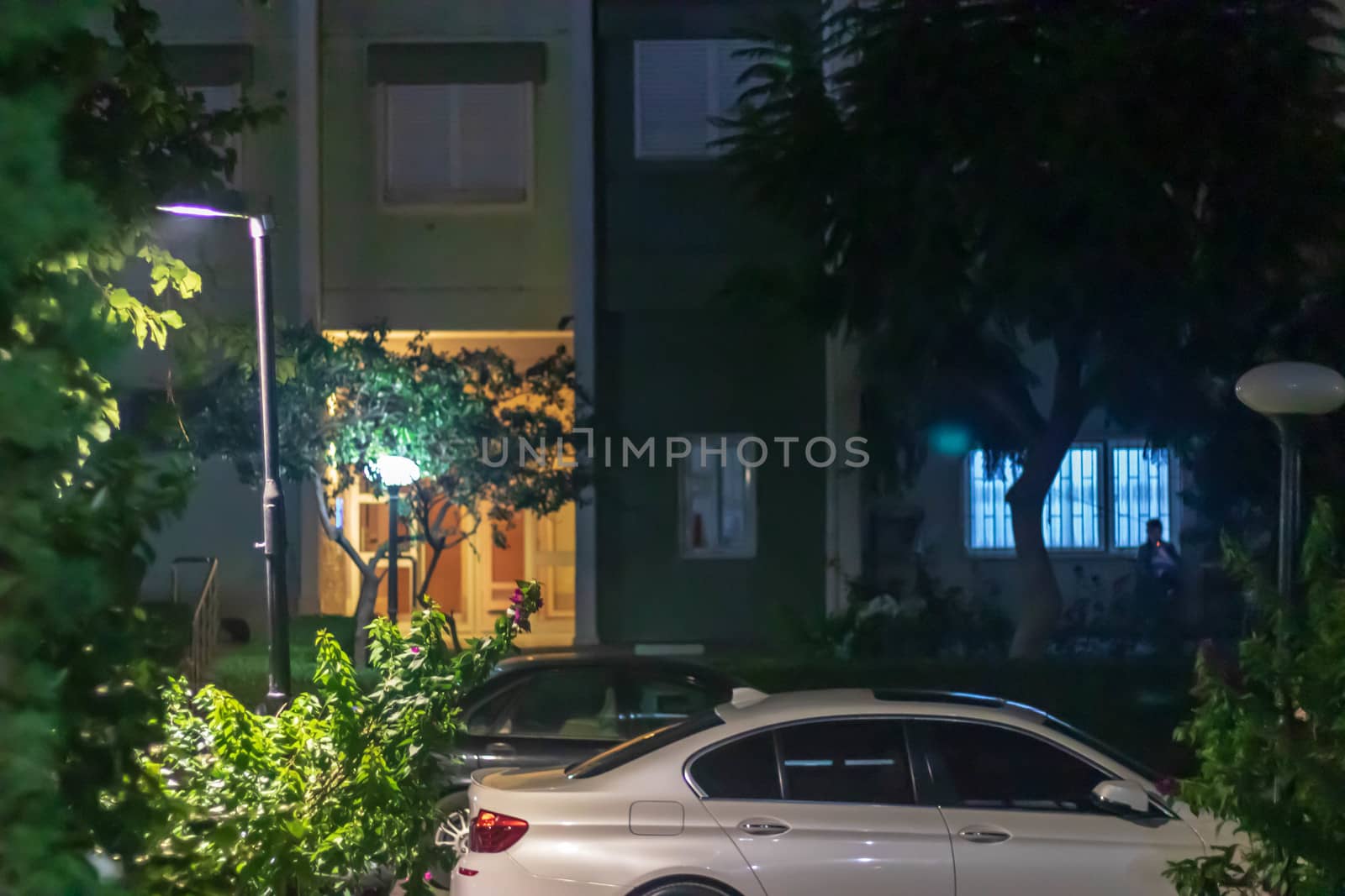 a night shoot of front of a building - there is a white car and some trees. photo has taken at izmir/turkey.