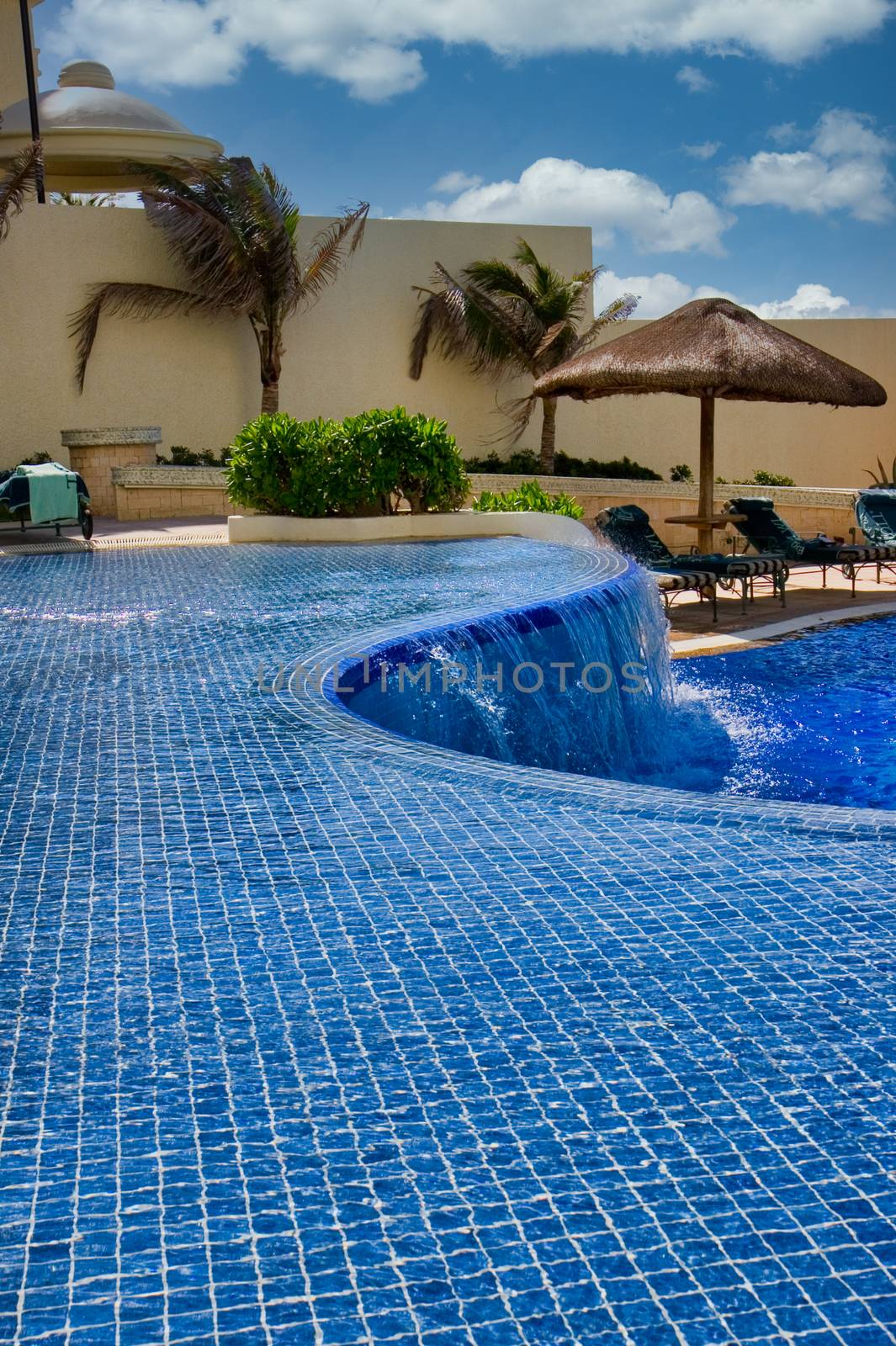 A curved pool and waterfall at a tropical resort hotel