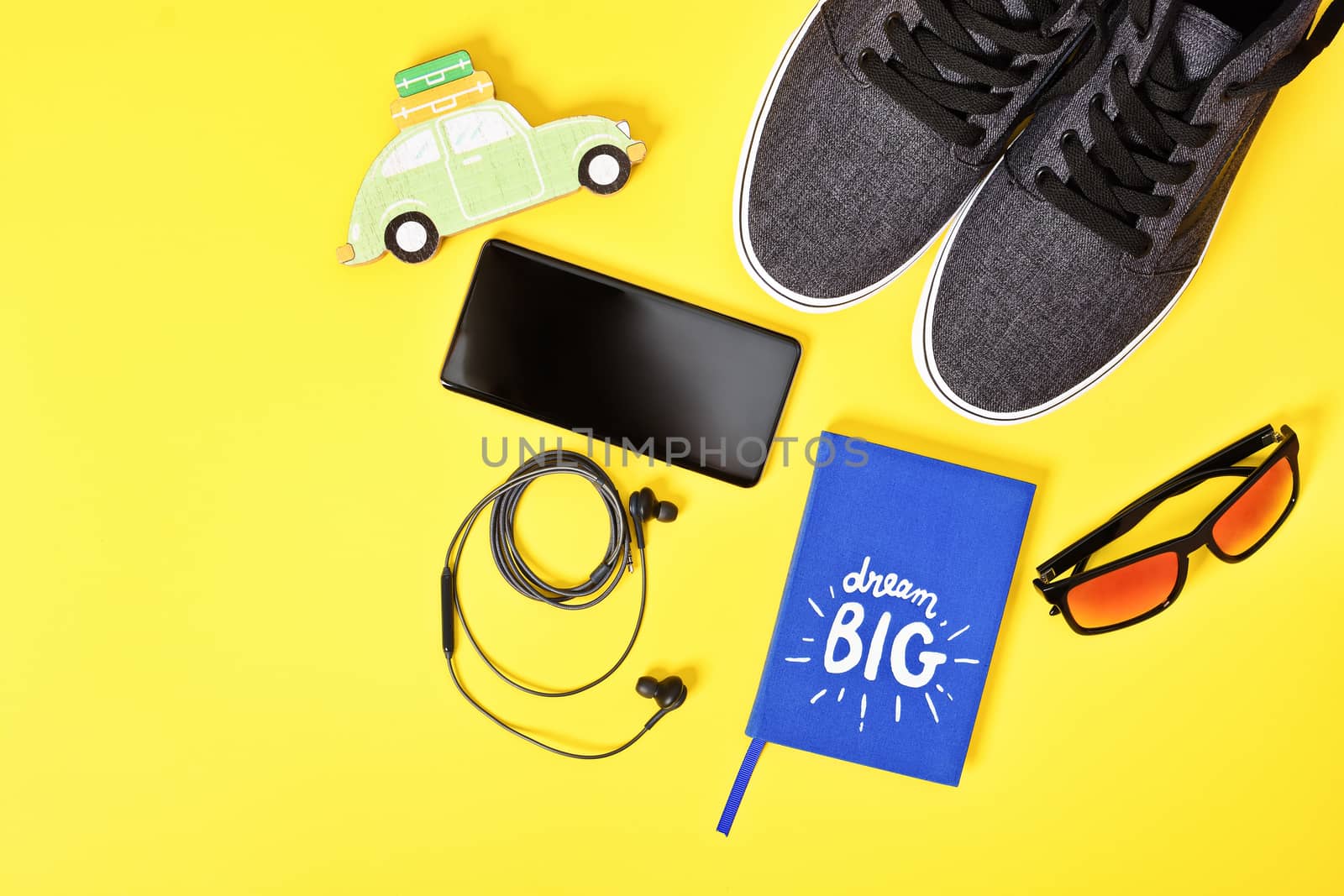 Travel planning, vacation and tourism concept. Top view of traveler's essential accessories including sneakers, sunglasses, smartphone, earphones and a Dream Big notepad on yellow background. Flat lay, copy space.