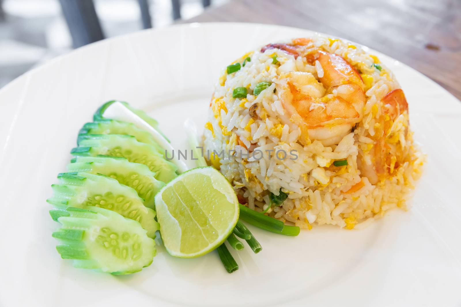 Thai traditional shrimp and egg fried rice served with sliced cucumber green onion and piece of lime on white ceramic dish
