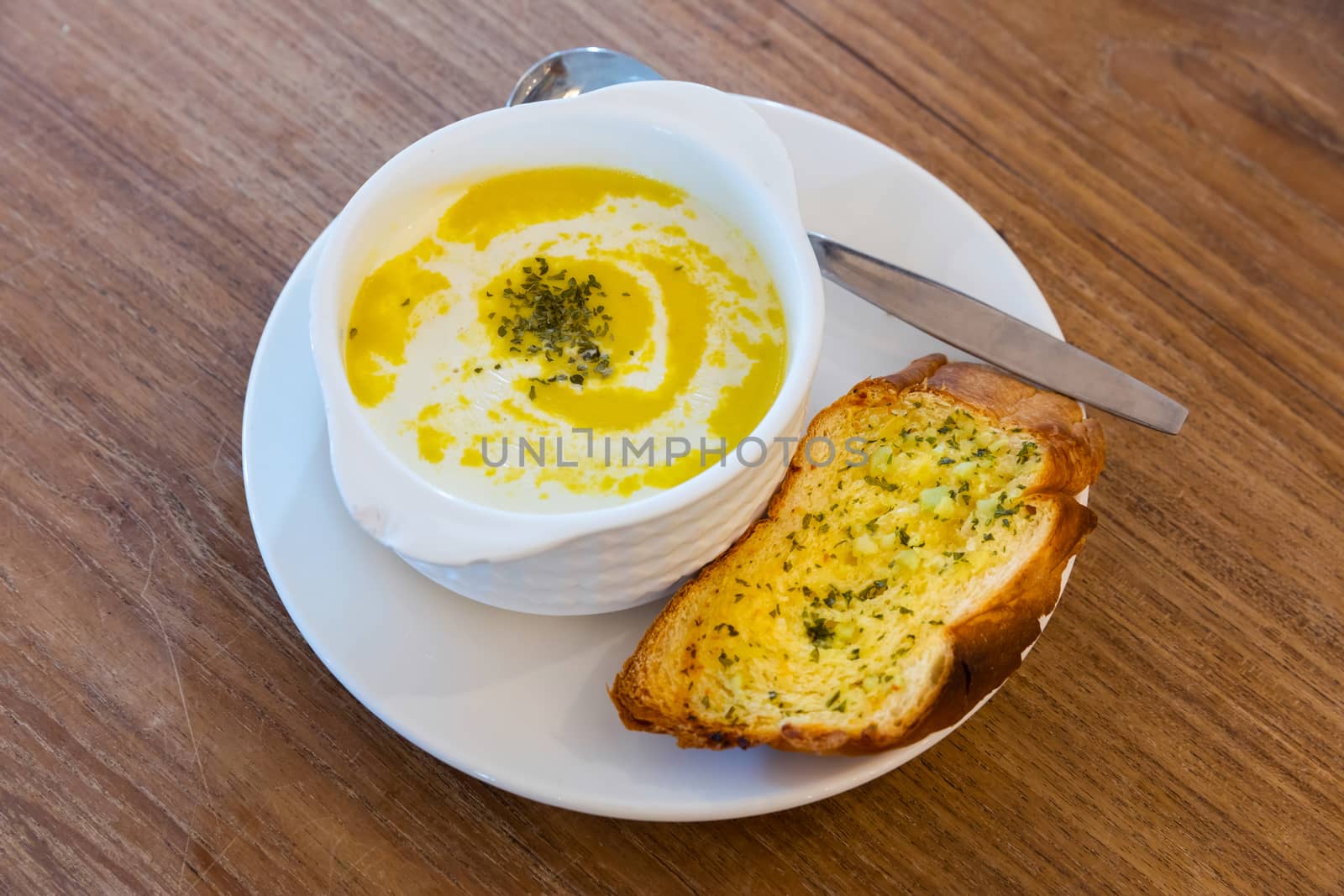Close up corn soup with oregano leaves and garlic bread in white ceramic cup on wooden table background