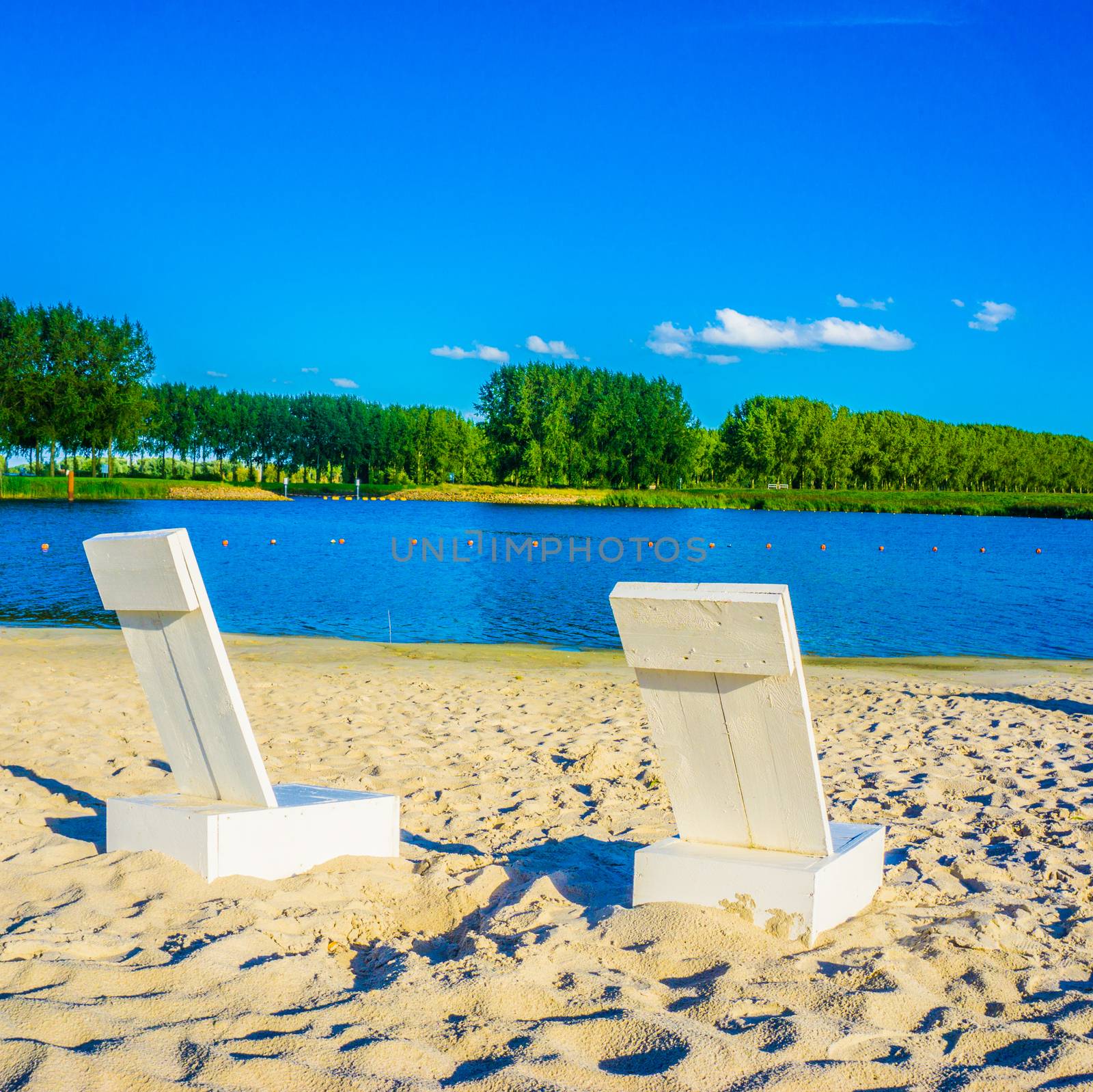 two white beach chairs at a sand beach lake landscape by charlottebleijenberg