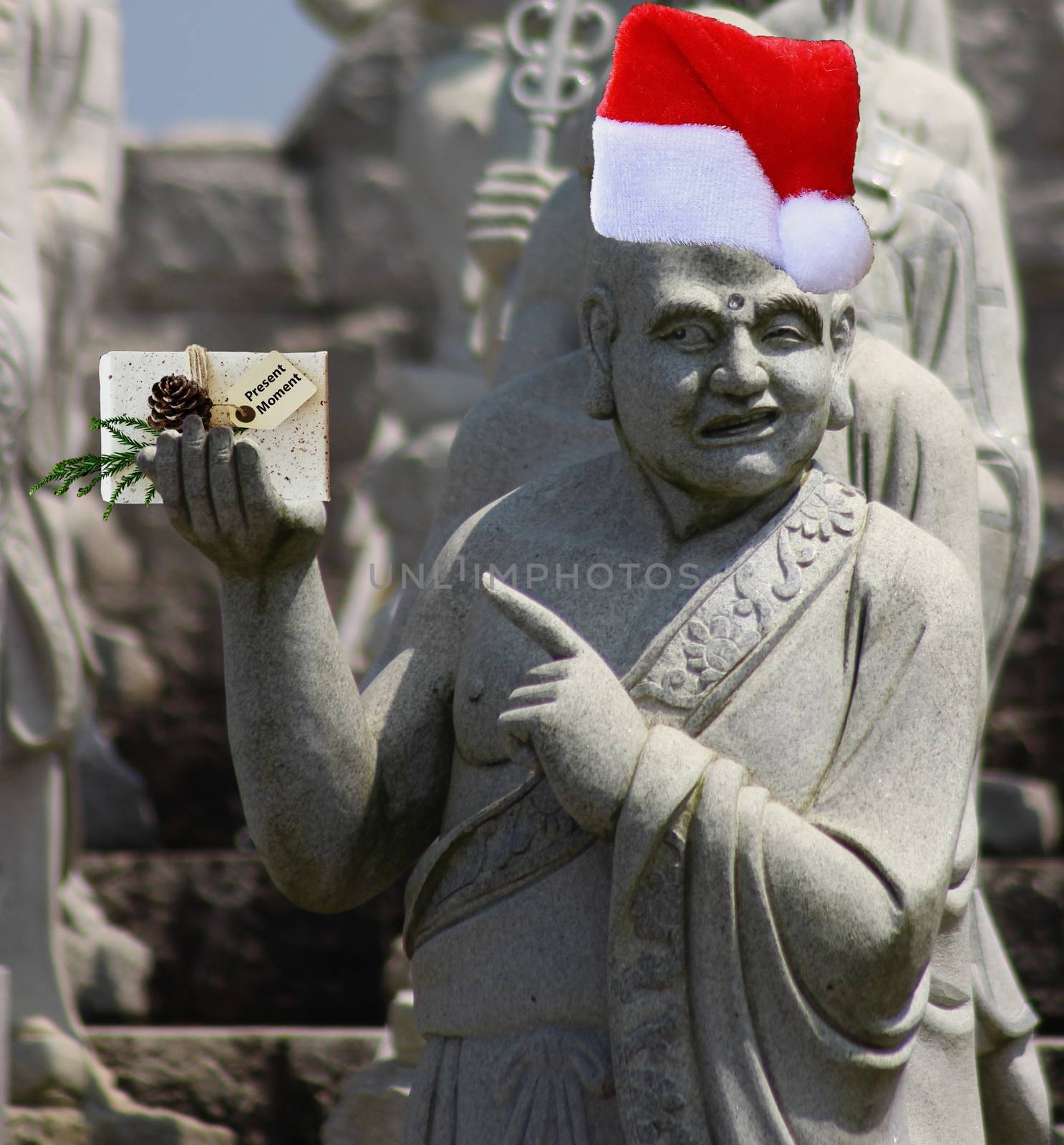 Christmas buddhist monk statue pointing at a gift that says present moment and wearing a santa claus hat by charlottebleijenberg