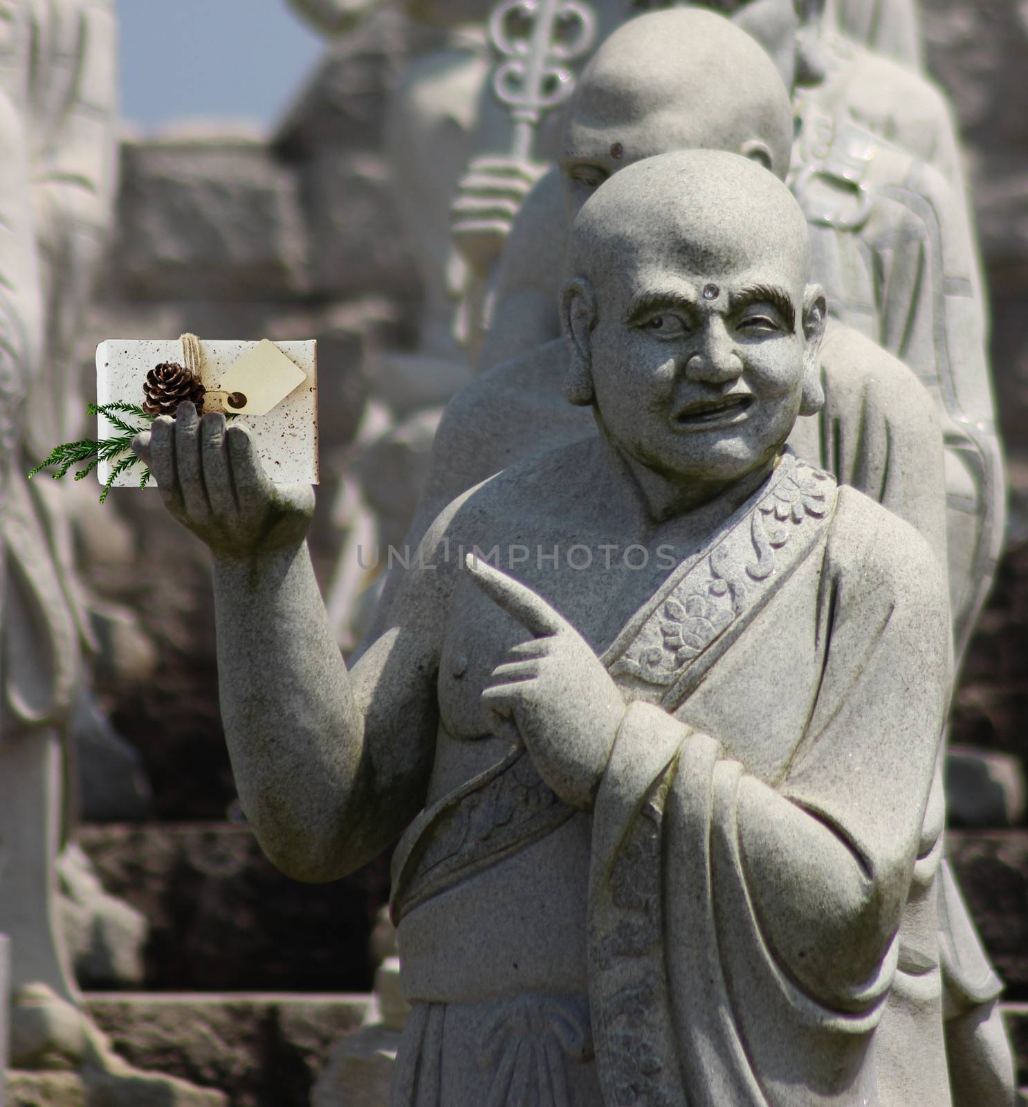 Christmas Buddhist monk statue holding a present with a blank card and pointing at it by charlottebleijenberg