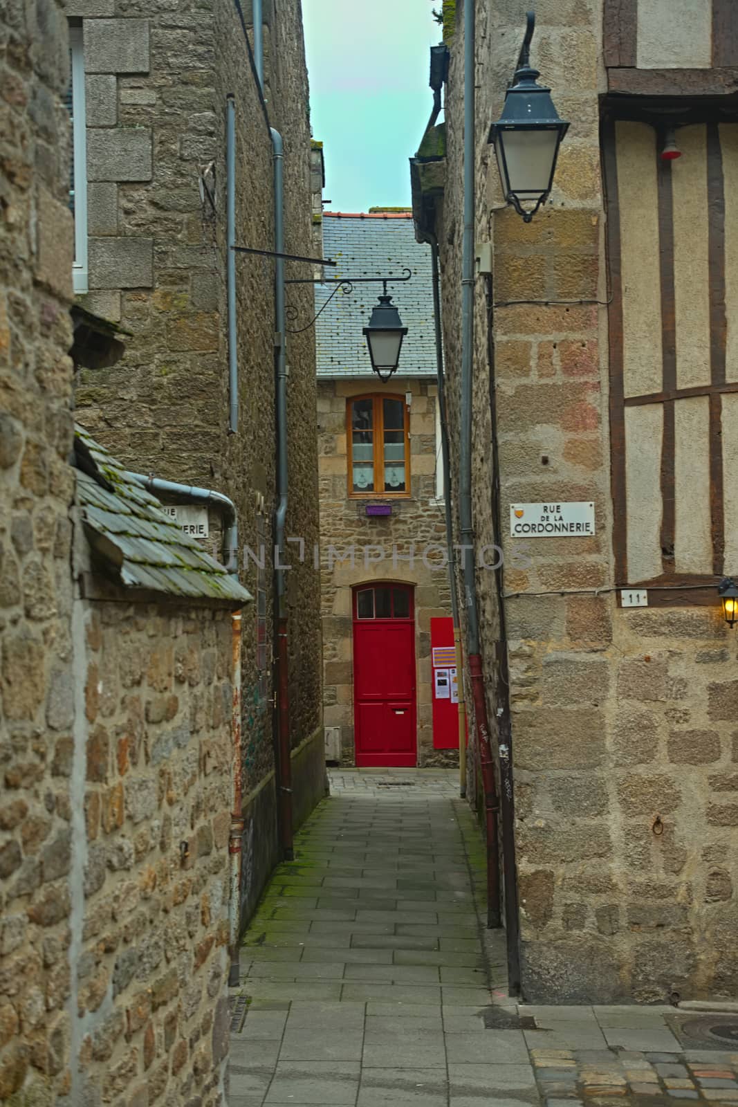 Narrow passage between two traditional stone buildings with red entrance door ahead by sheriffkule