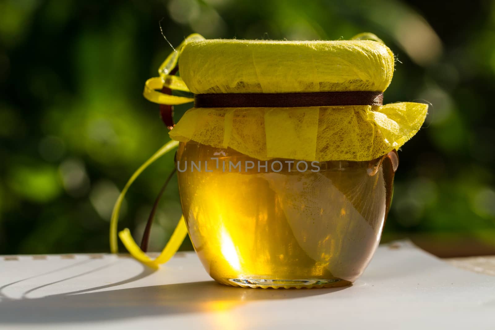 Jar with honey on table against nature background by maggee