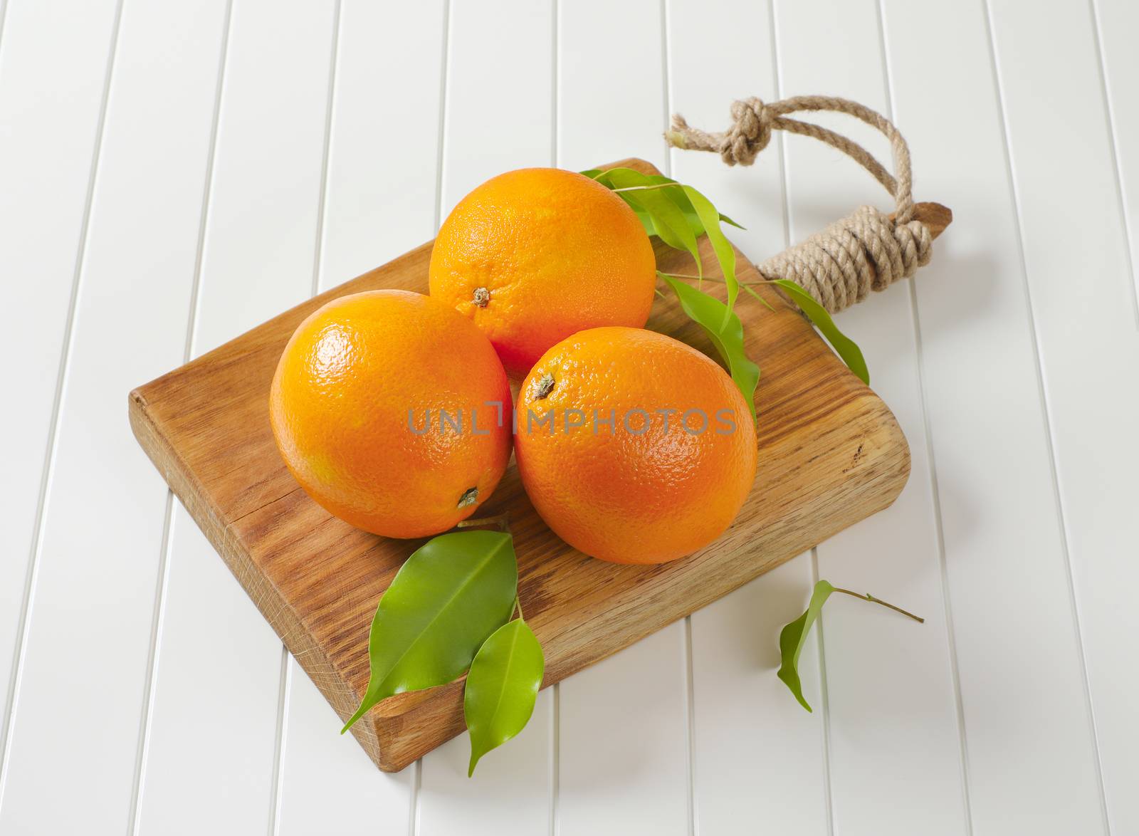 Three whole ripe oranges and leaves on cutting board
