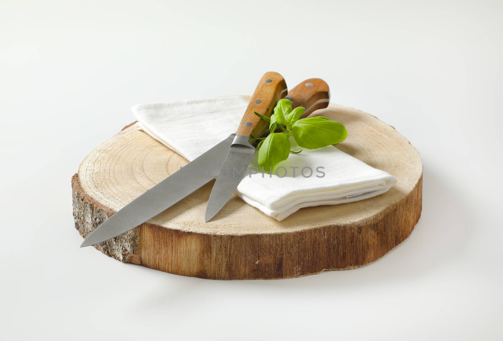 Set of two sharp pointed tip kitchen knives and white napkin on round wood slab