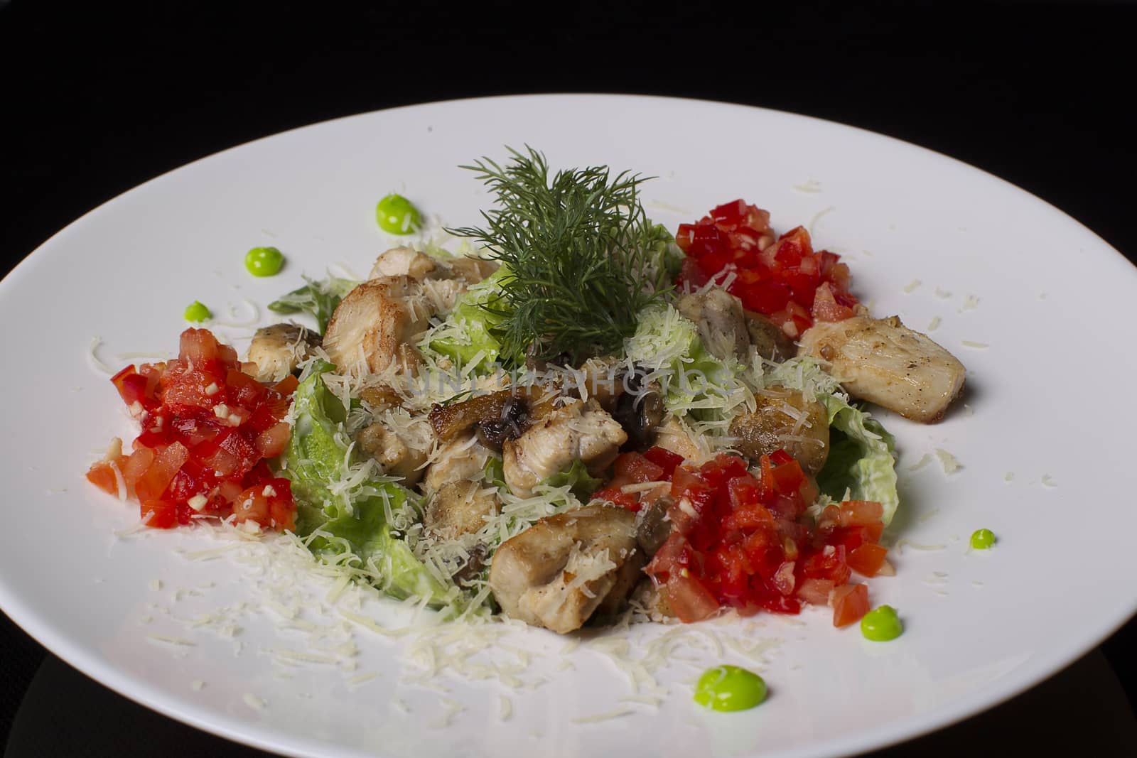On a white plate salad of meat, tomatoes, lettuce, dill, sprinkled with cheese, on a black background. by Sviatlana