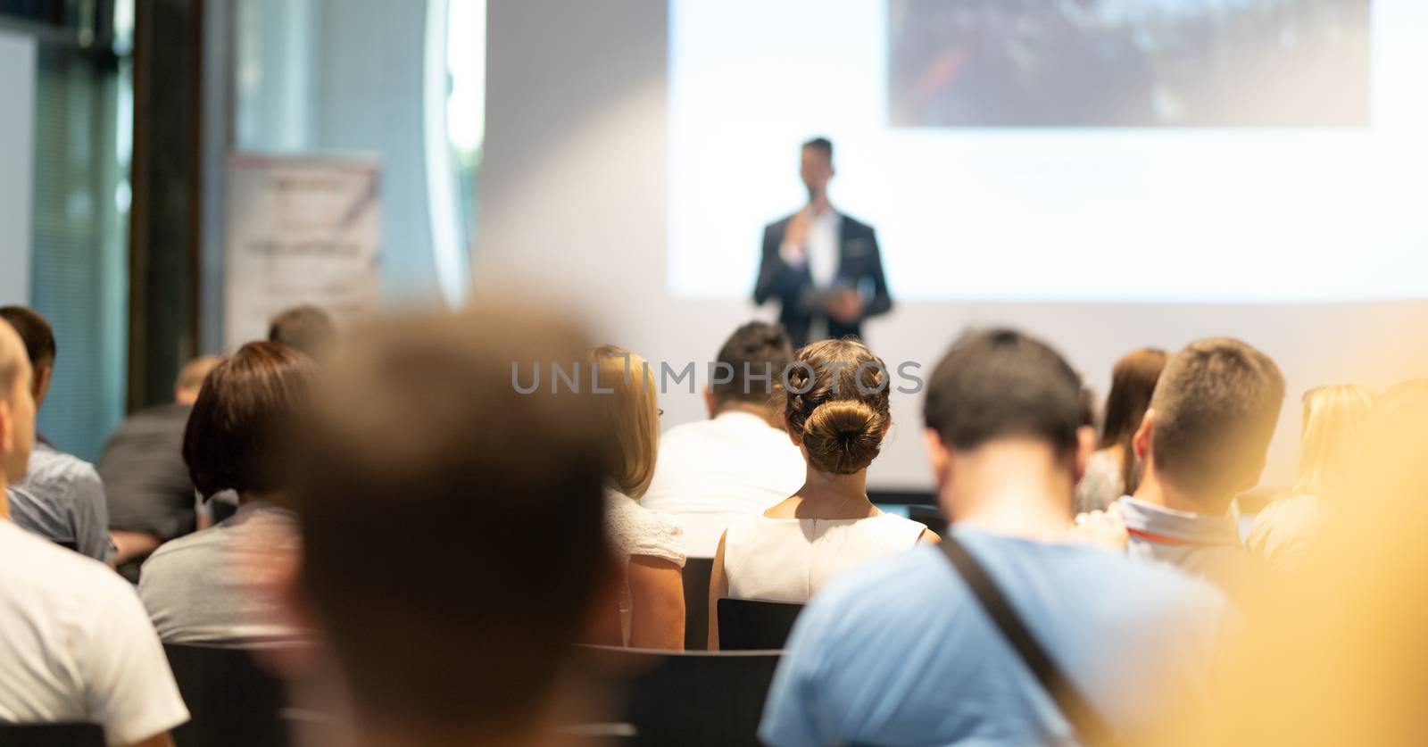 Male speaker giving a talk in conference hall at business event. Audience at the conference hall. Business and Entrepreneurship concept. Focus on unrecognizable people in audience.