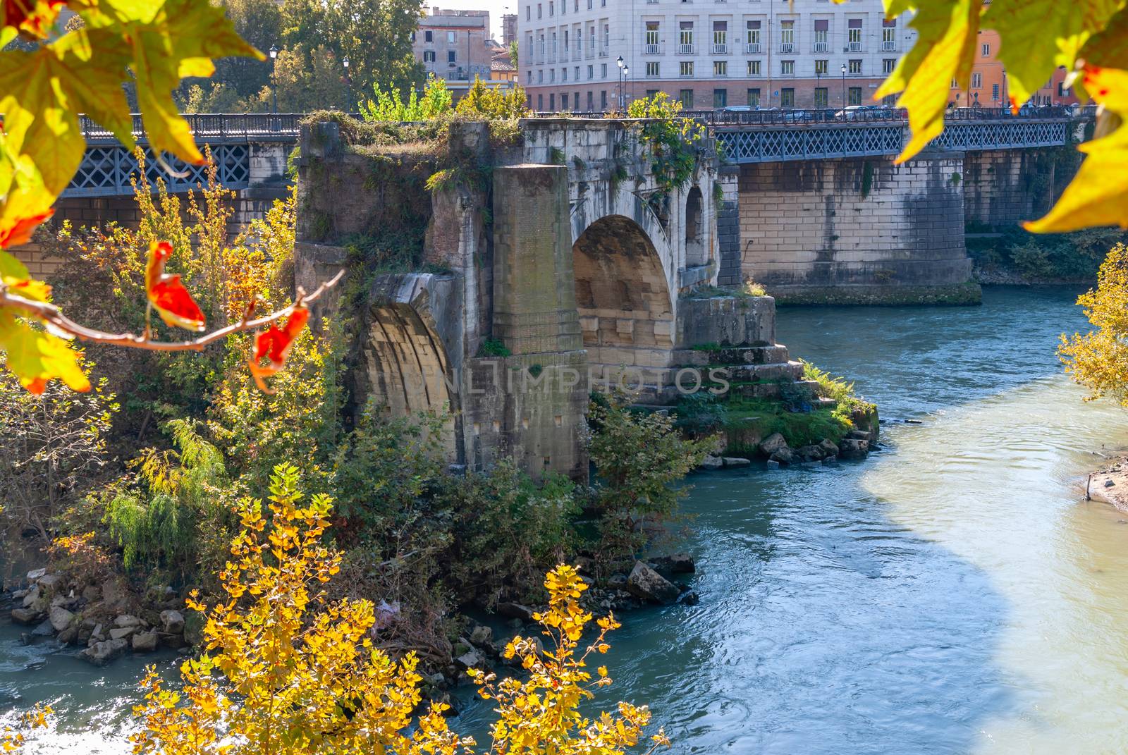 The remains of the ancient Ponte Rotto or Pons Aemilius Broken Bridge with Isola Tiberina Tevere Island in the background, Roma, Italy