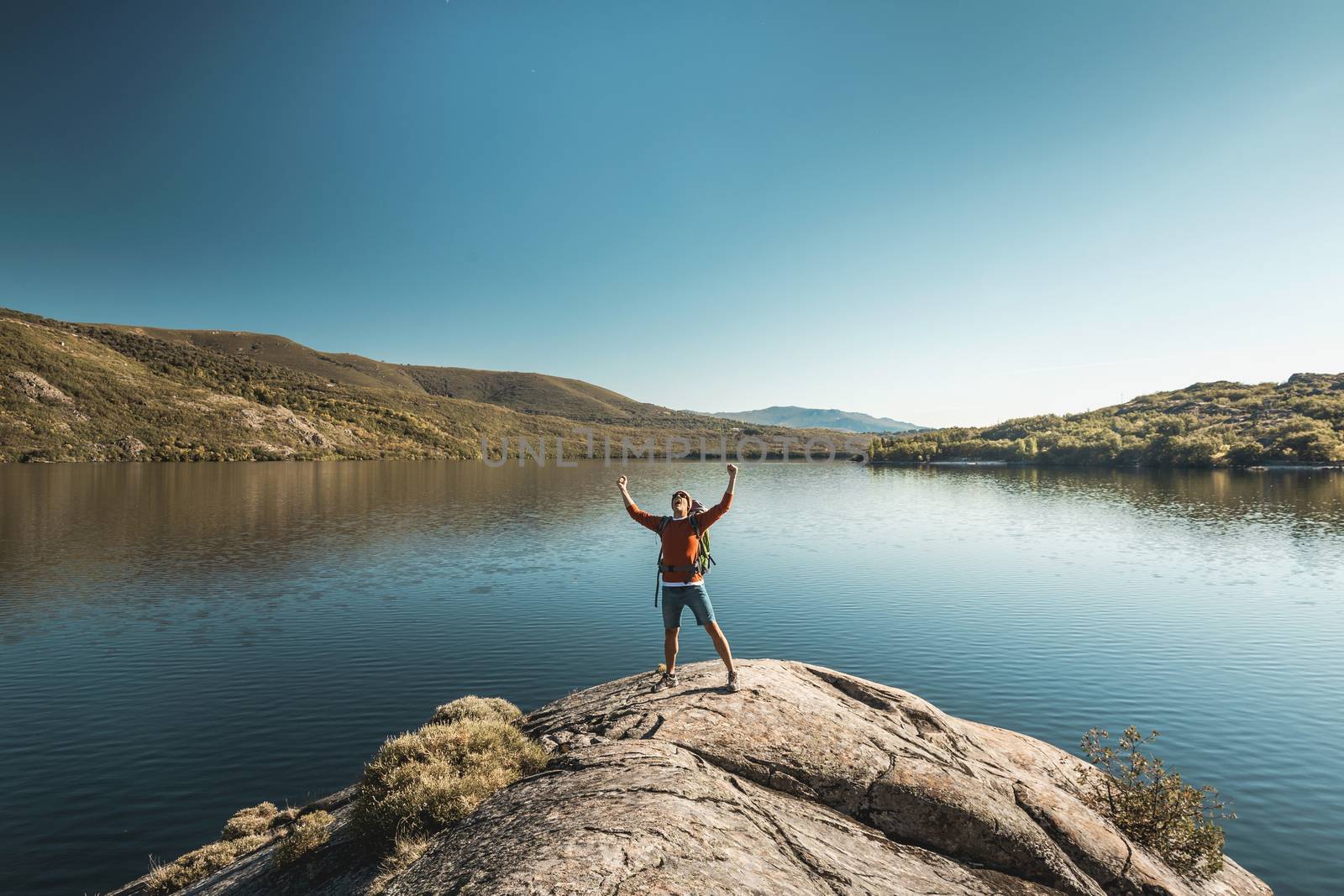 Shot of a man hiking near a beautiful lake with arsm raised