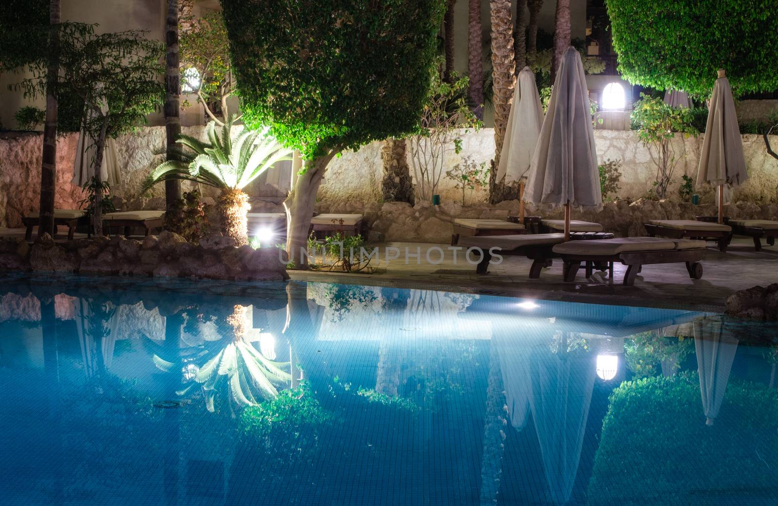 blue water pool and green palm trees with street lamps at night without people in sharm el sheikh egypt
