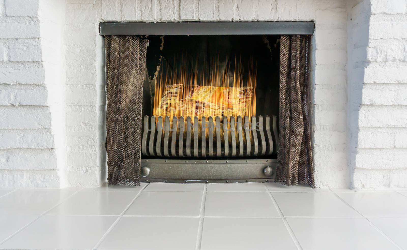 lighted and burning fireplace in retro style but with a modern look background architecture is of white brick stones and white tiling by charlottebleijenberg