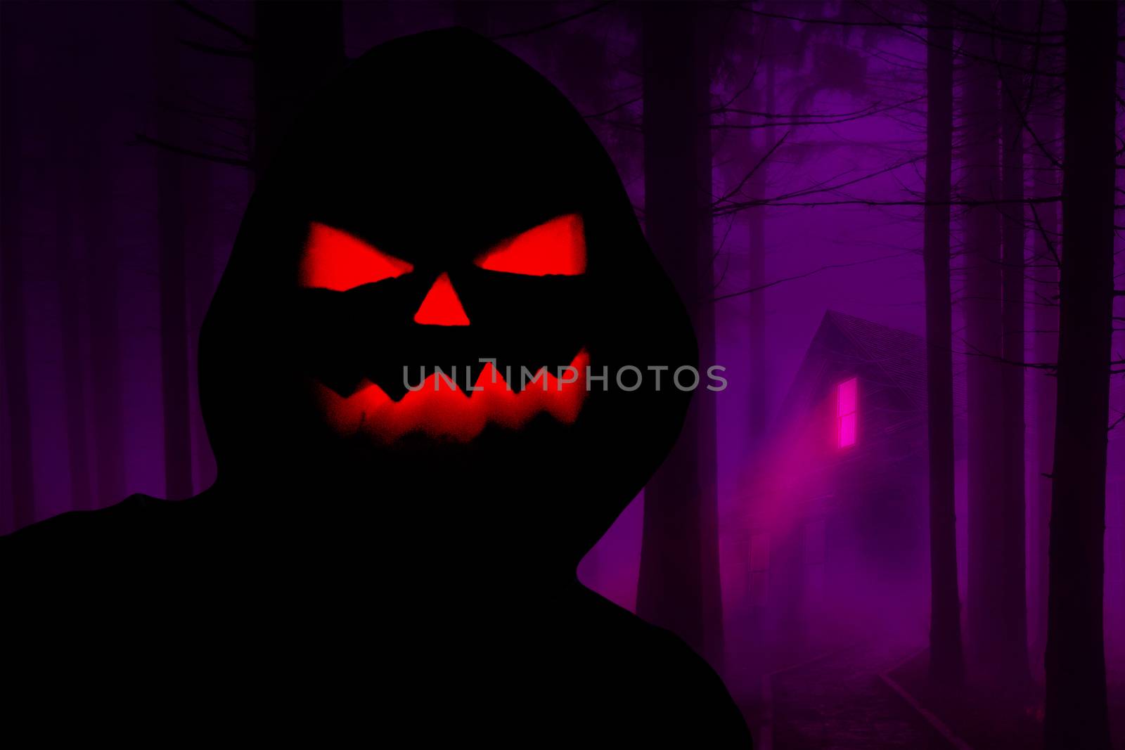 Halloween creepy hooded silhouette with a evil pumpkin face standing in a horror forest with a haunted house in the background