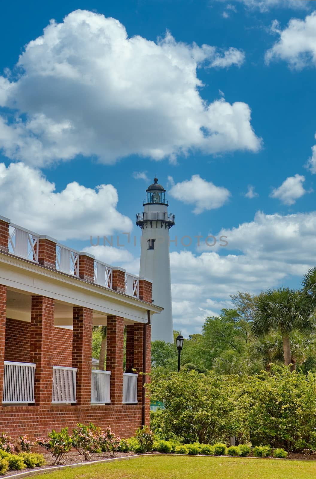 A lighthouse on the horizon past a brick building and trees