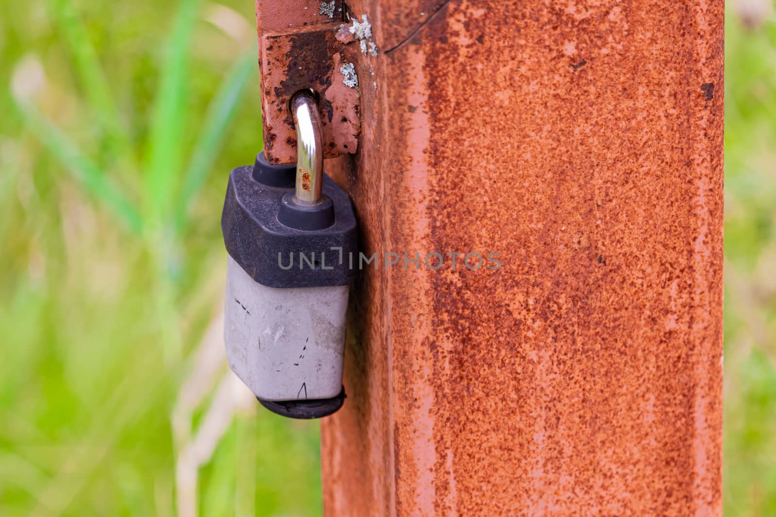A rusty post along a footpath has a padlock on it, restricting access to an electrical line inside.